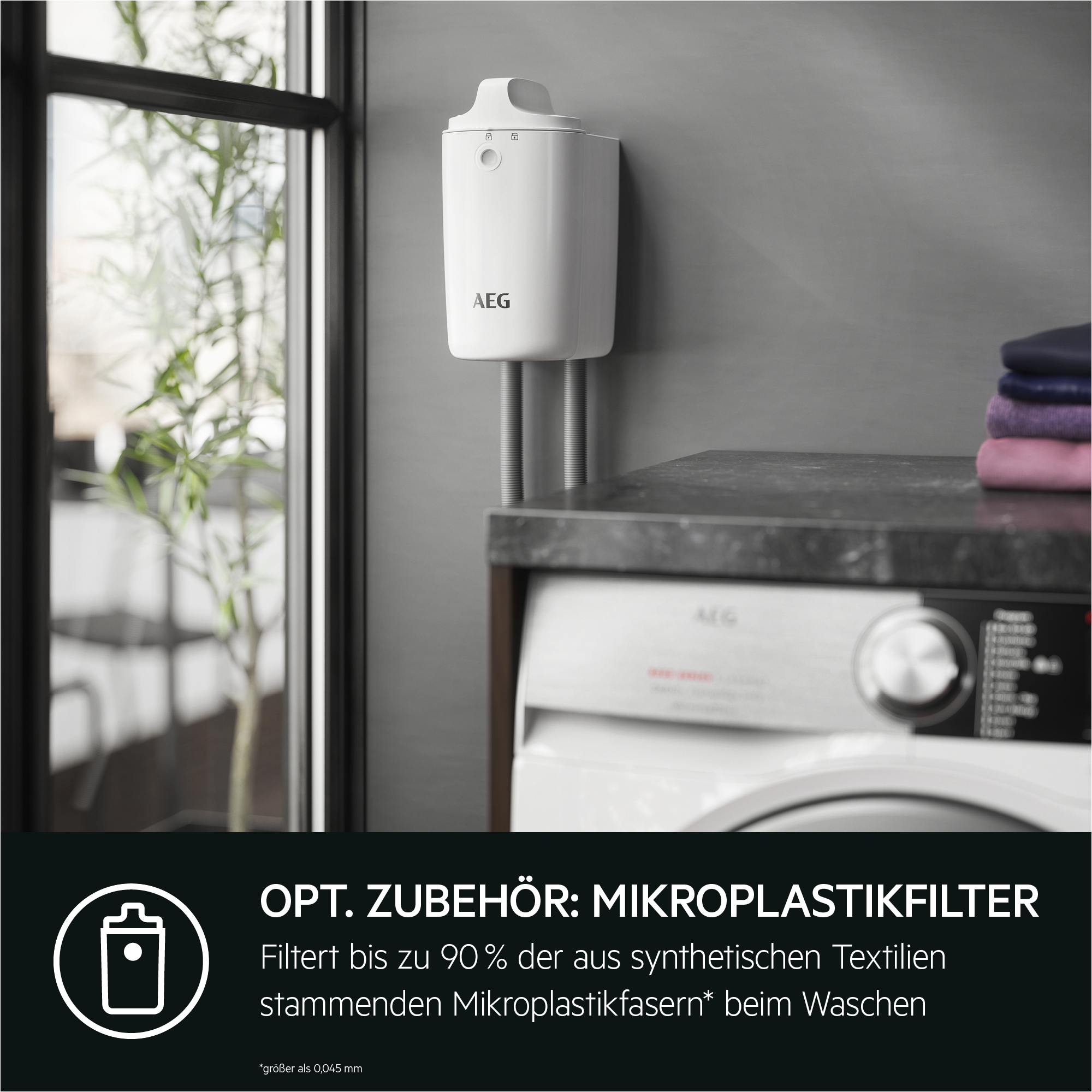 Ein weißer AEG-Mikroplastikfilter an der Wand. Im Hintergrund eine Waschmaschine. Links ein Fenster.