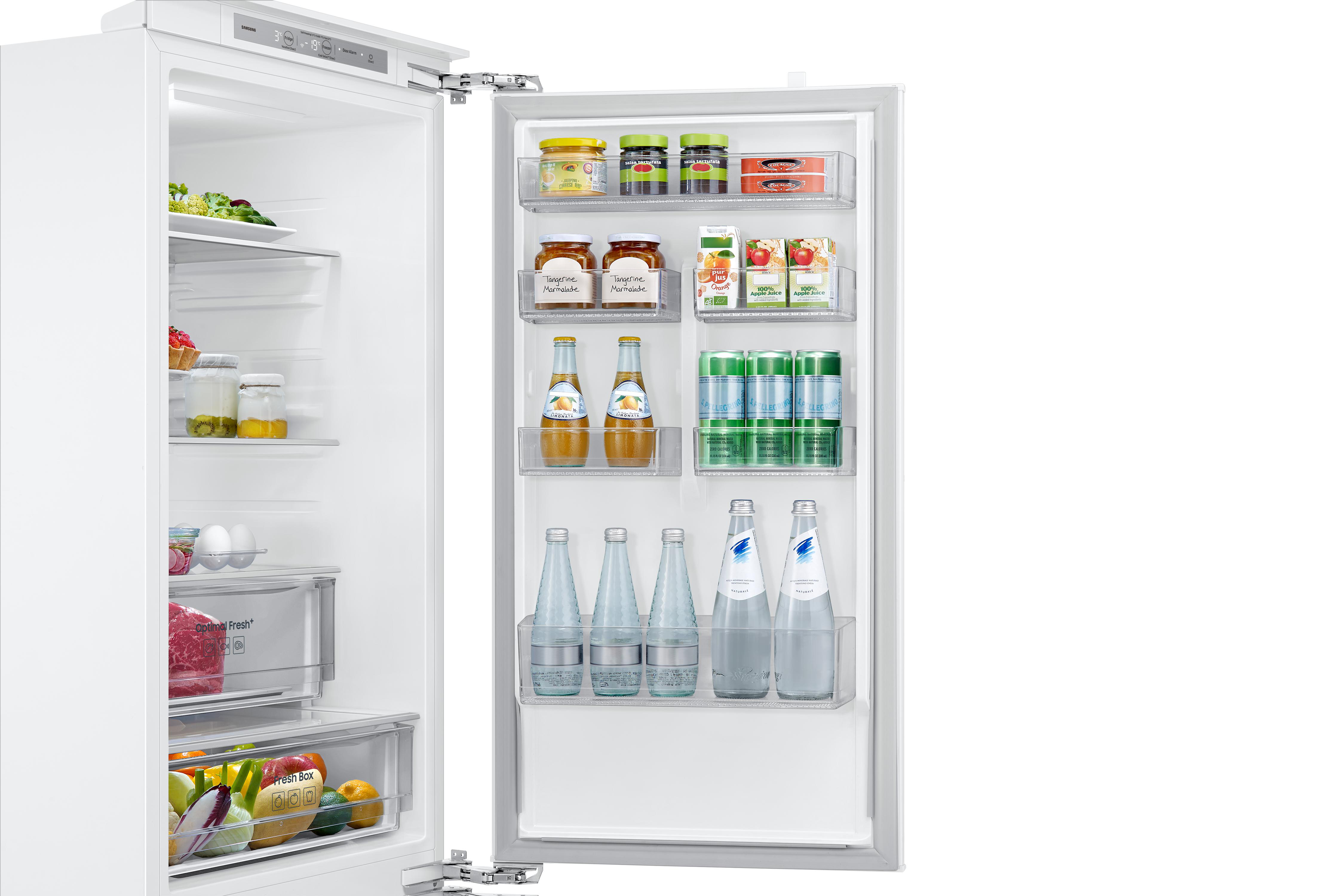 Offener Kühlschrank mit Lebensmitteln: Obst, Gemüse, Getränke, Marmeladen und Gläser. Weißer Innenraum mit Regalen.