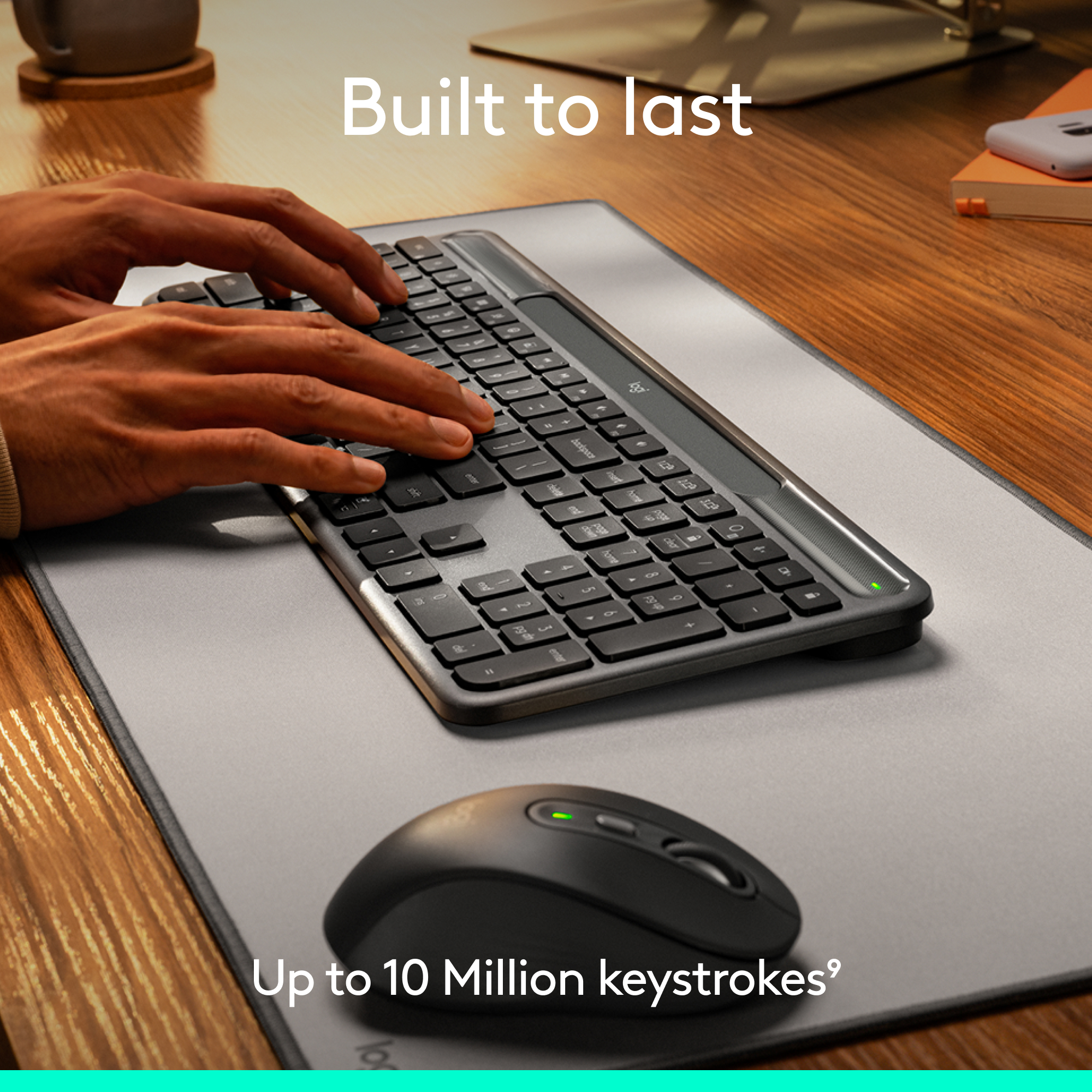 Mains tapant sur un clavier noir, souris noire sur un tapis gris. Table en bois. Texte : 'Built to last', 'Up to 10 Million keystrokes'.