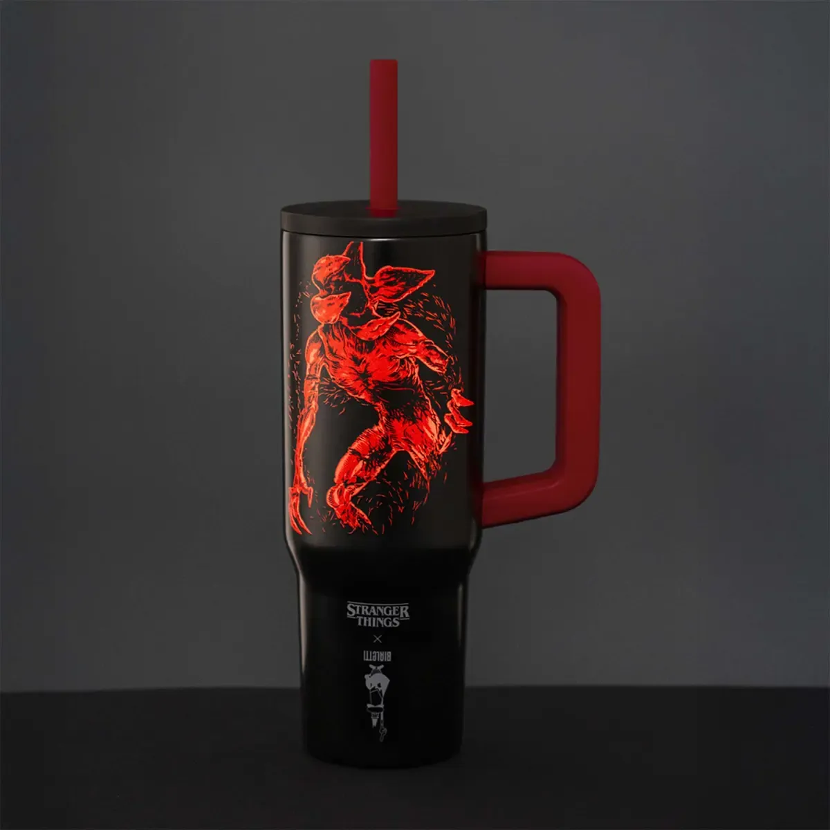 Fekete bögre piros fogantyúval és szívószállal. Piros Demogorgon illusztrációt és Stranger Things márkajelzést tartalmaz.