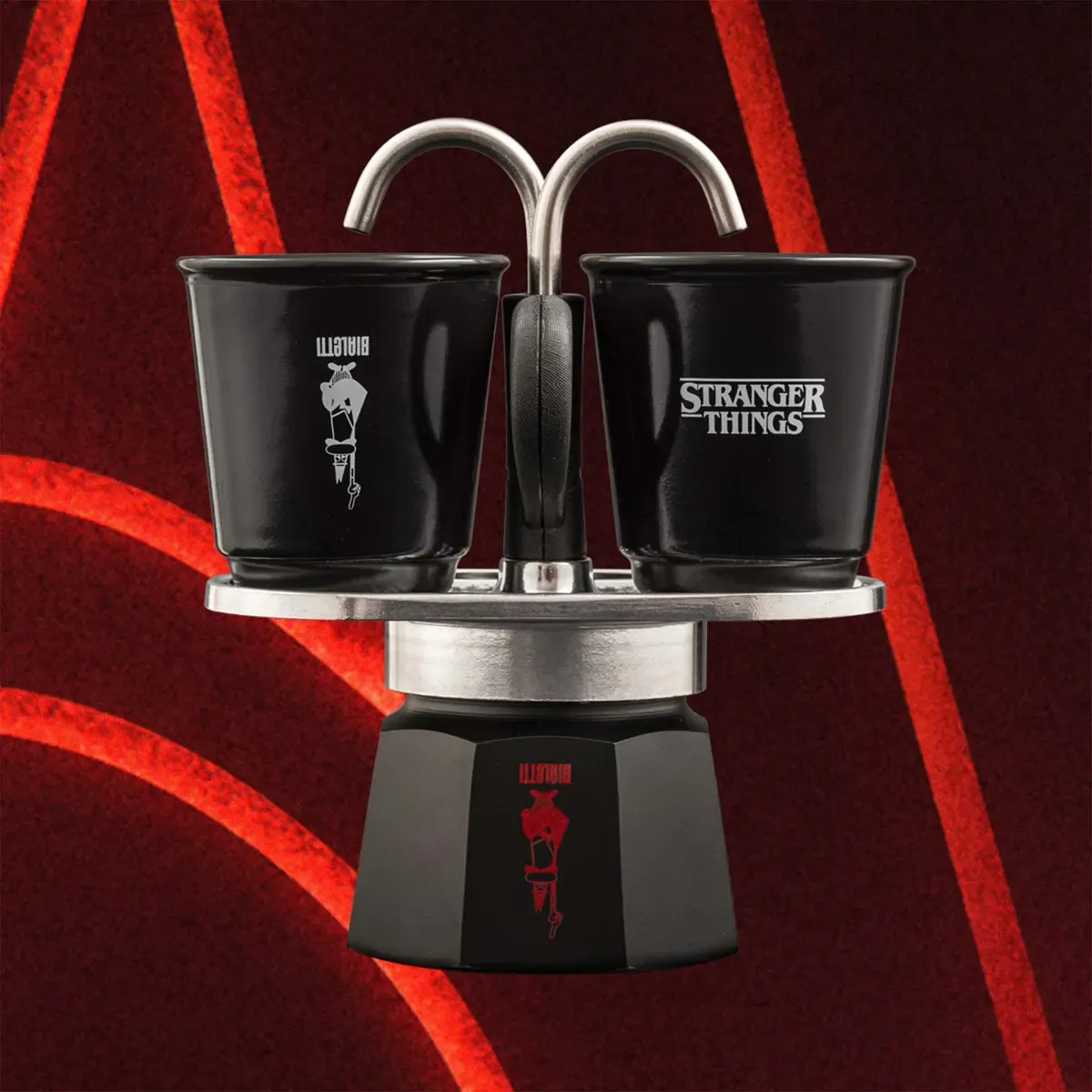 Fekete eszpresszó készítő két csészével. Az egyiken 'Bialetti', a másikon 'Stranger Things' felirat. Piros, ívelt vonalas háttér.