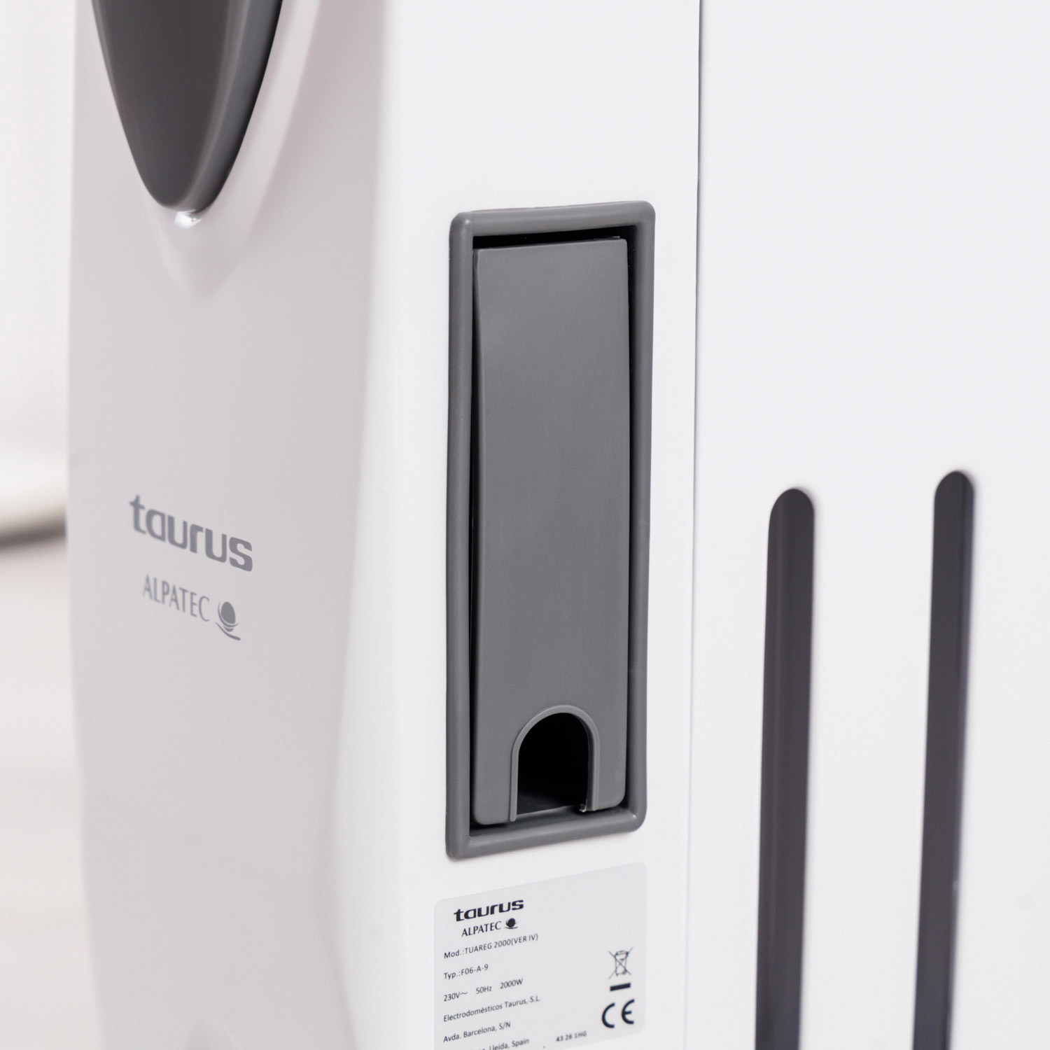 Primer plano de un electrodoméstico blanco y gris con el logotipo de Taurus Alpatec. Se ve una manija gris y una etiqueta con especificaciones.