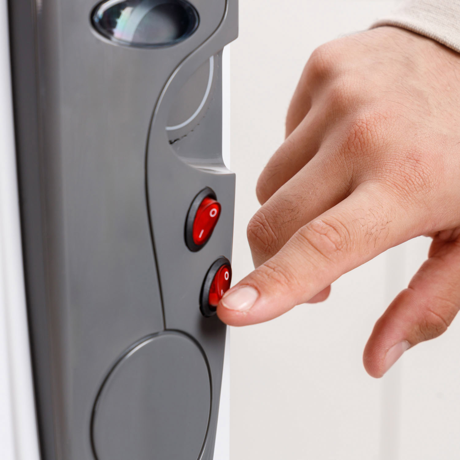 Una mano enciende un interruptor rojo en un aparato gris. El interruptor está etiquetado con un cero. El fondo es blanco.