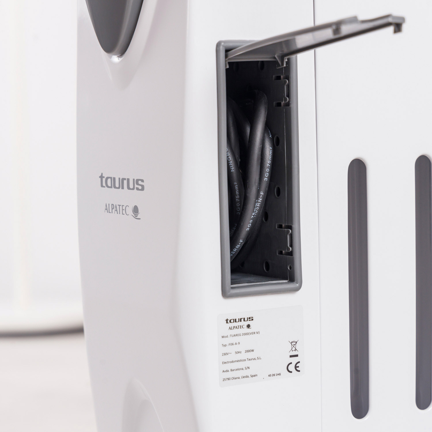 Un electrodoméstico blanco y gris. El compartimento abierto revela cables negros. El electrodoméstico tiene una etiqueta de marca con texto y una marca CE.