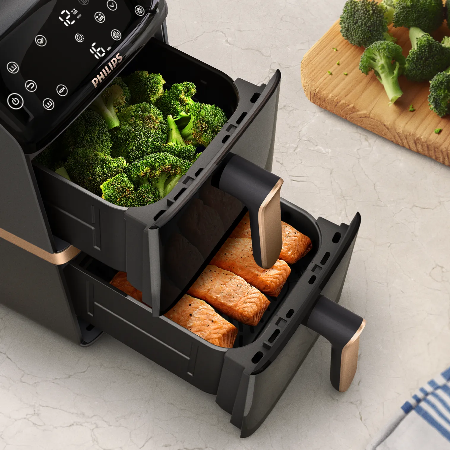 Un airfryer avec du brocoli et du saumon. Brocoli dans le tiroir du haut, saumon dans le bas. Brocoli sur une planche en bois en arrière-plan.