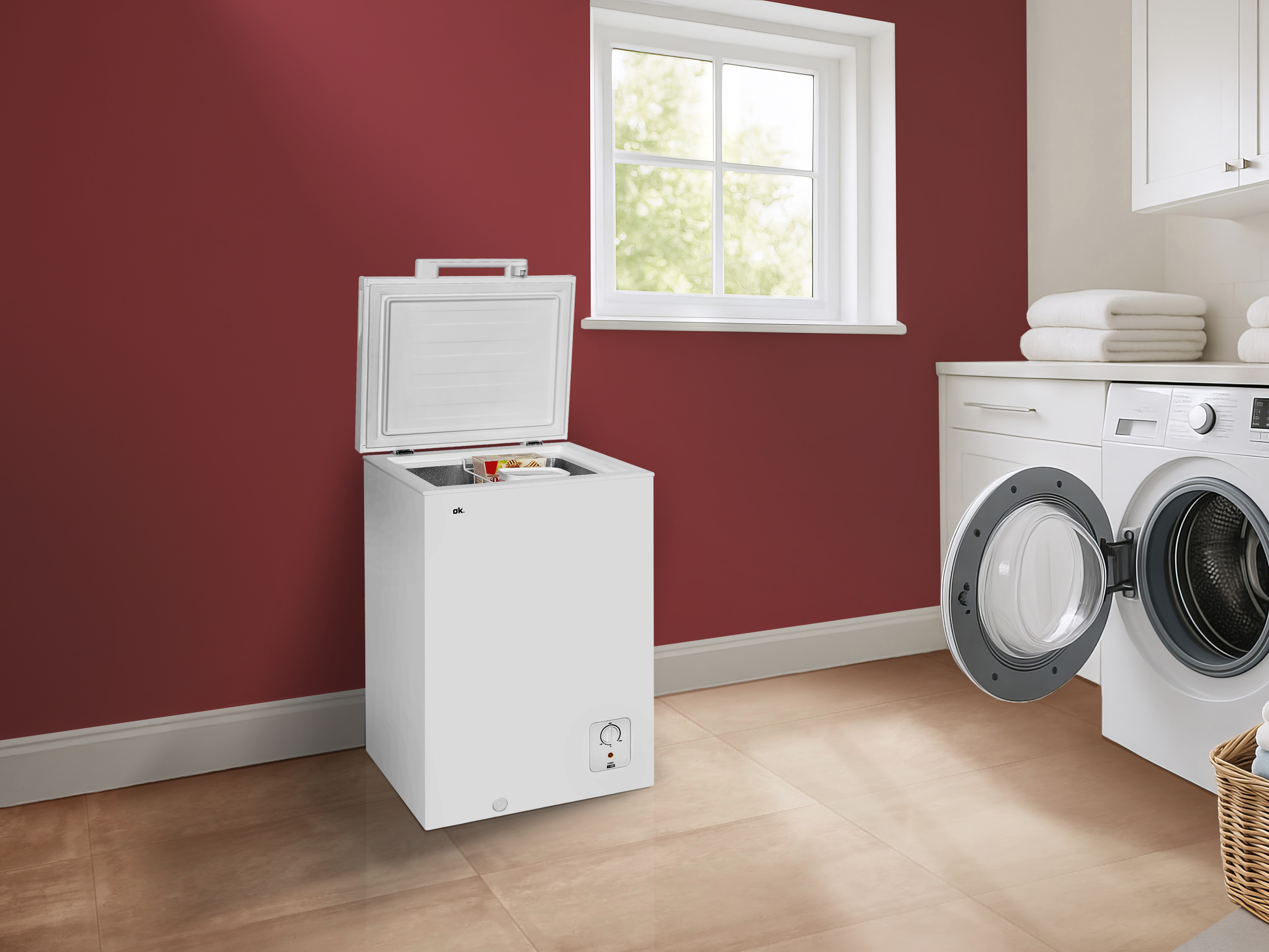 Ein weißer Gefrierschrank mit offenem Deckel steht in der Nähe einer Waschmaschine und eines Fensters.