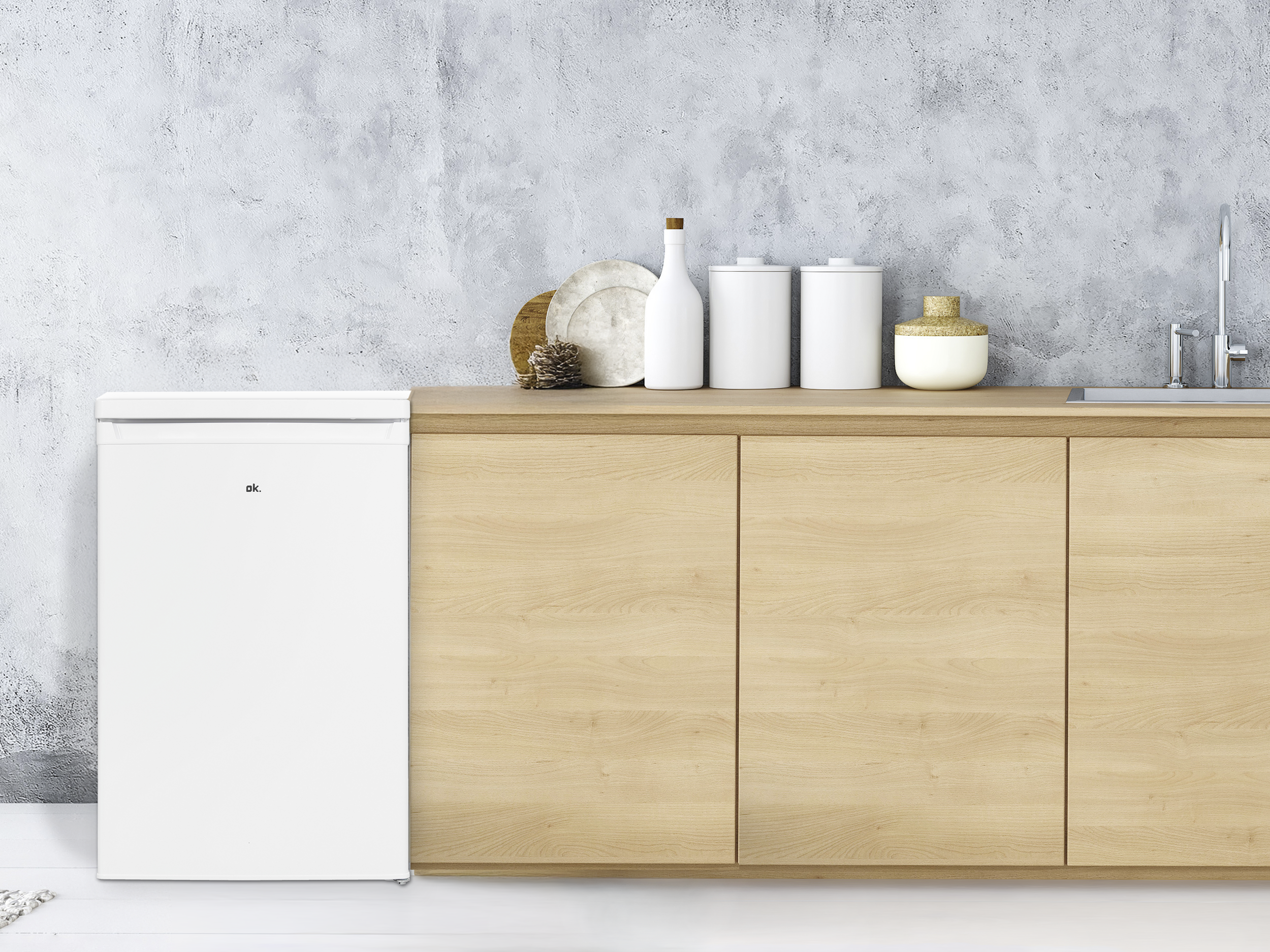 Ein weißer Kühlschrank steht neben einer Holztheke mit Küchenutensilien und einem Waschbecken vor einer strukturierten Wand.
