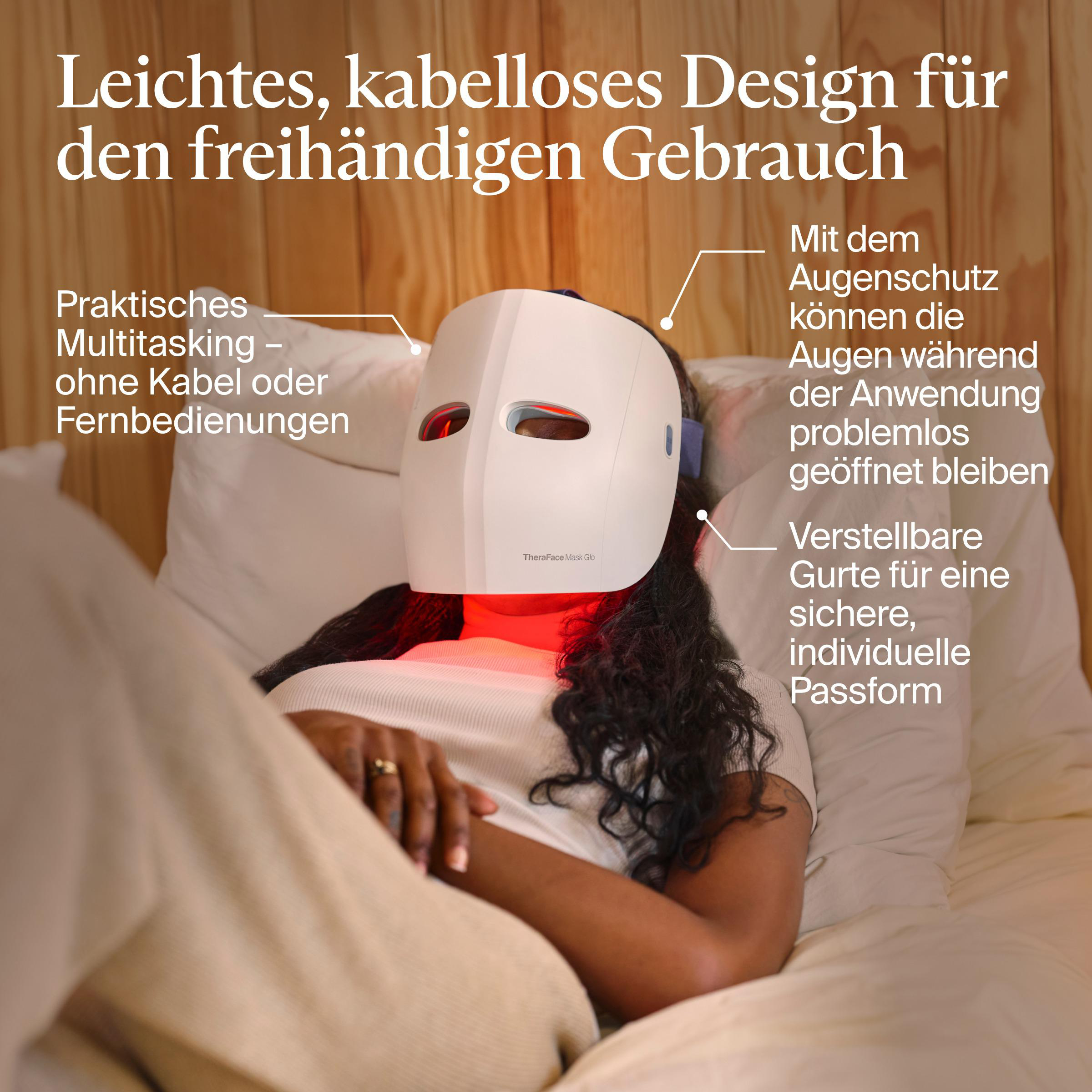 Eine Person liegt mit einer weißen Gesichtsmaske mit roten Lichtern auf Kissen. Die Szene ist drinnen.