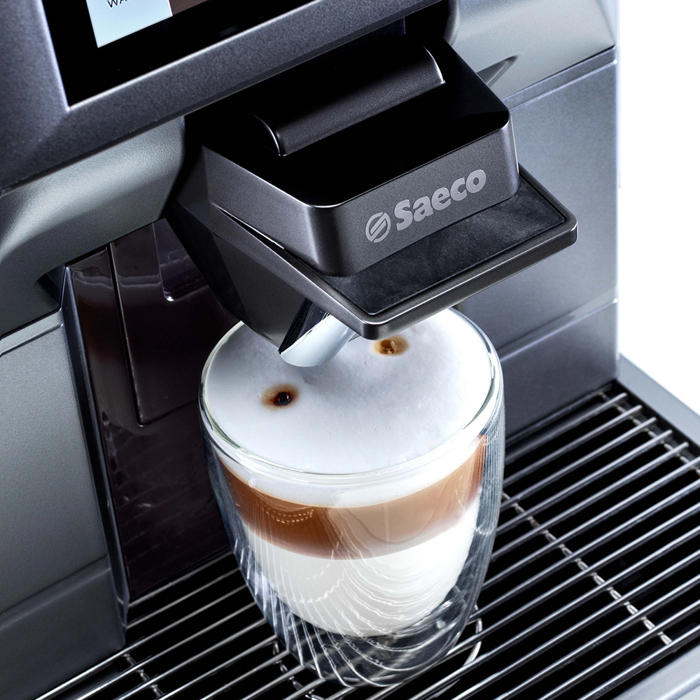 Egy kávéfőző egy lattét ad ki egy átlátszó pohárba. A latte tejből és kávéból áll, tetején habbal.
