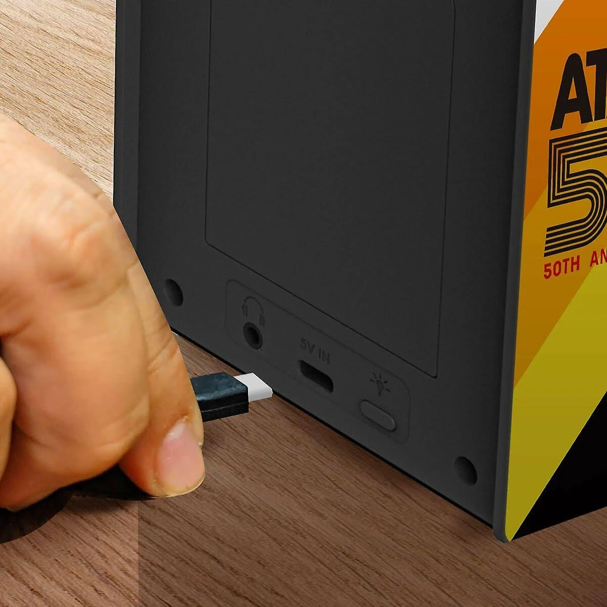 Una mano inserta un cable USB en un dispositivo negro. El dispositivo tiene puertos y un lado con un logo amarillo y negro.