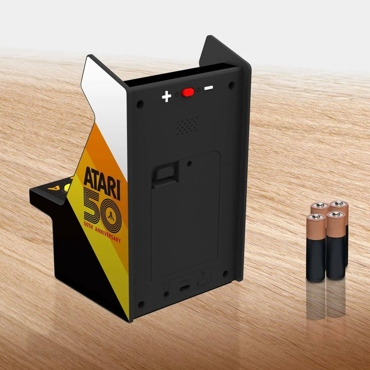 Mini máquina arcade Atari. Diseño negro y blanco con detalles amarillos, logo '50th Anniversary'. Cuatro pilas a la derecha.