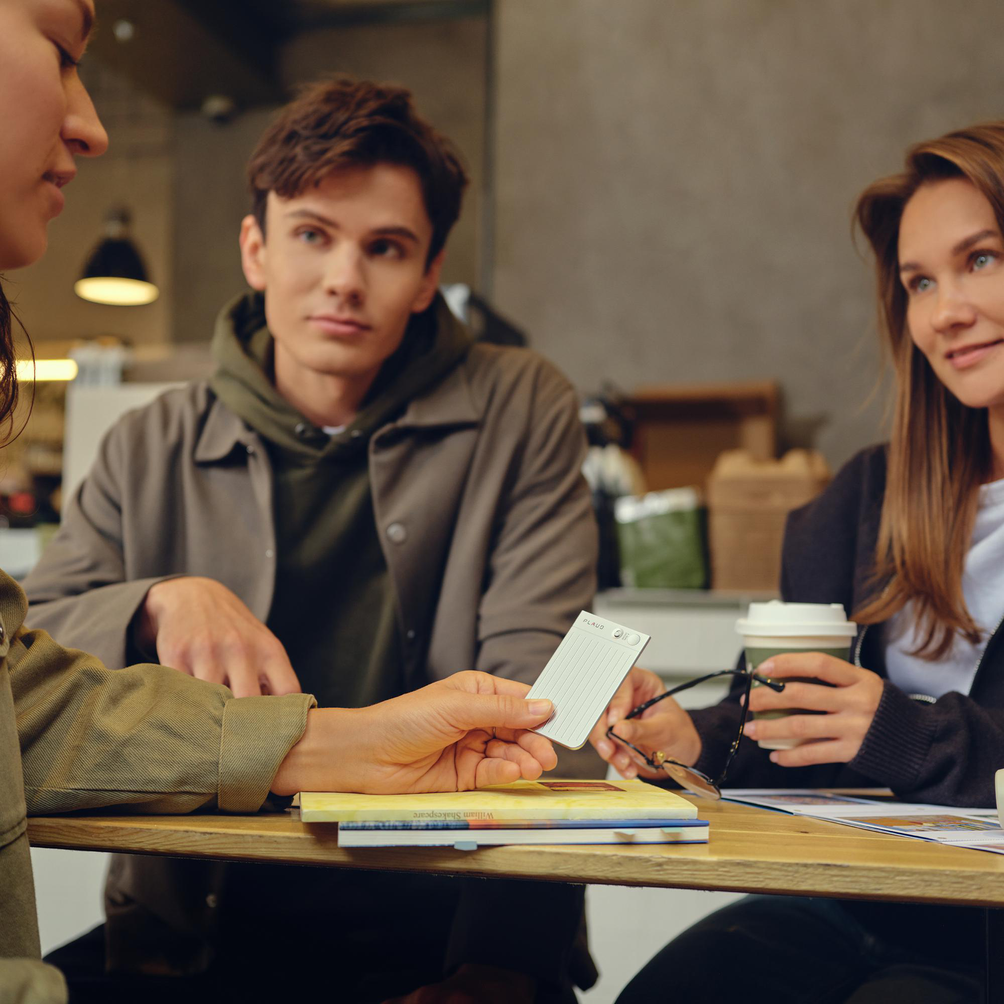 Drei Personen an einem Tisch. Eine Person hält eine Karte. Andere haben Kaffee und Gläser.