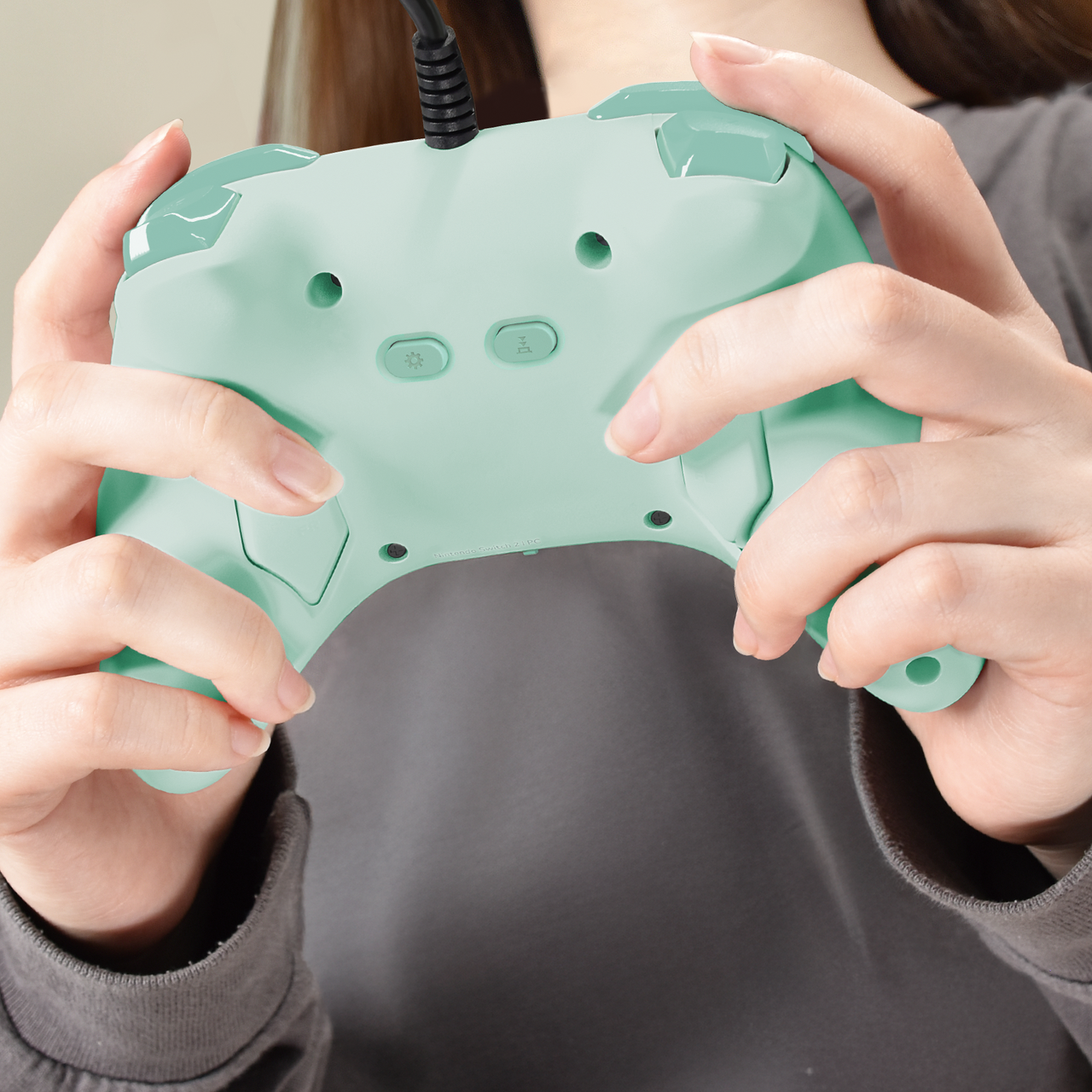 Une personne tient une manette de jeu vert menthe. La manette a des boutons et un câble noir. Mains visibles.