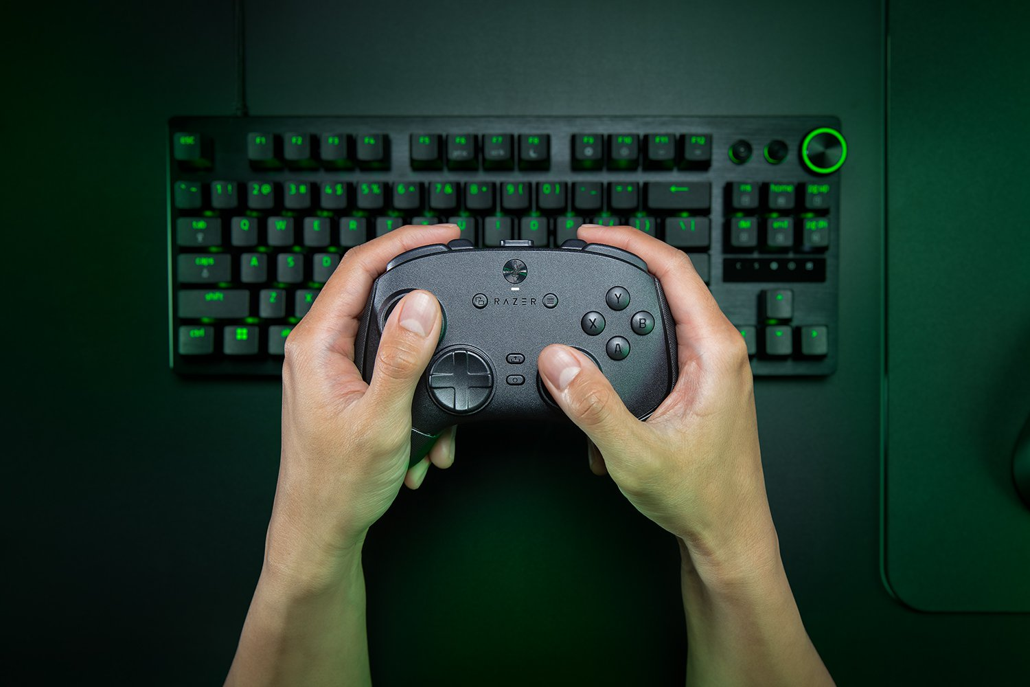 Hände halten einen Razer-Gaming-Controller, im Hintergrund eine schwarze Tastatur mit grün hinterleuchteten Tasten.