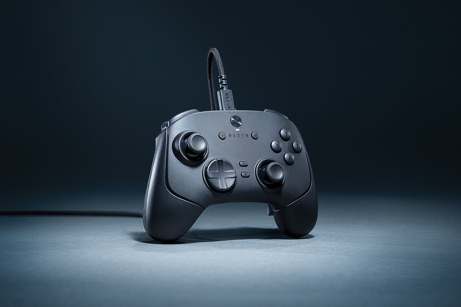 Un gamepad Razer nero è centrato. Sono visibili pulsanti, un D-pad e joystick. Un cavo si collega in alto.