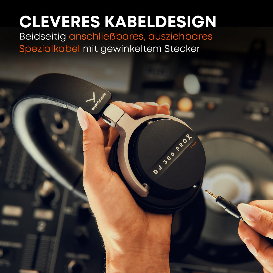 Eine Person hält einen schwarzen und silbernen Kopfhörer mit abnehmbarem Kabel. Im Hintergrund ist ein DJ-Mischpult zu sehen.
