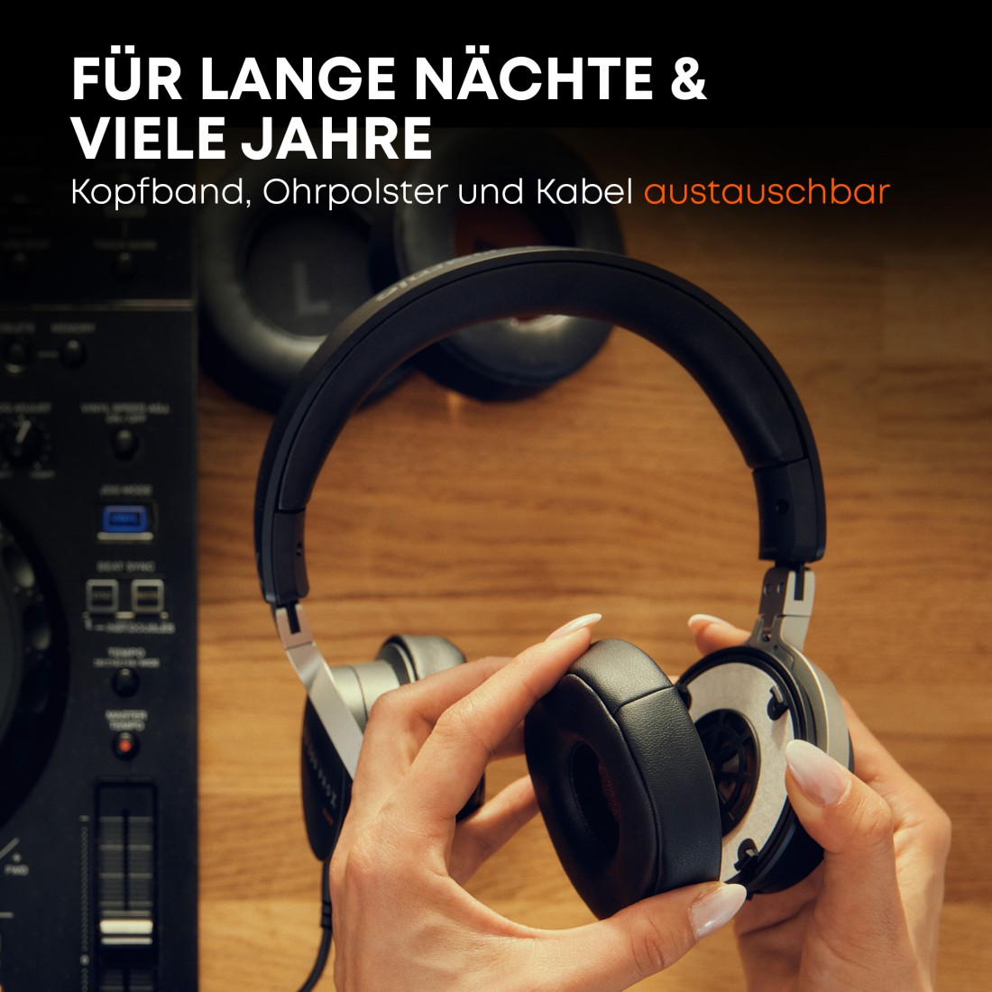 Hände halten schwarze Kopfhörer mit silbernen Akzenten. Im Hintergrund sind Holz und ein DJ-Mixer zu sehen.