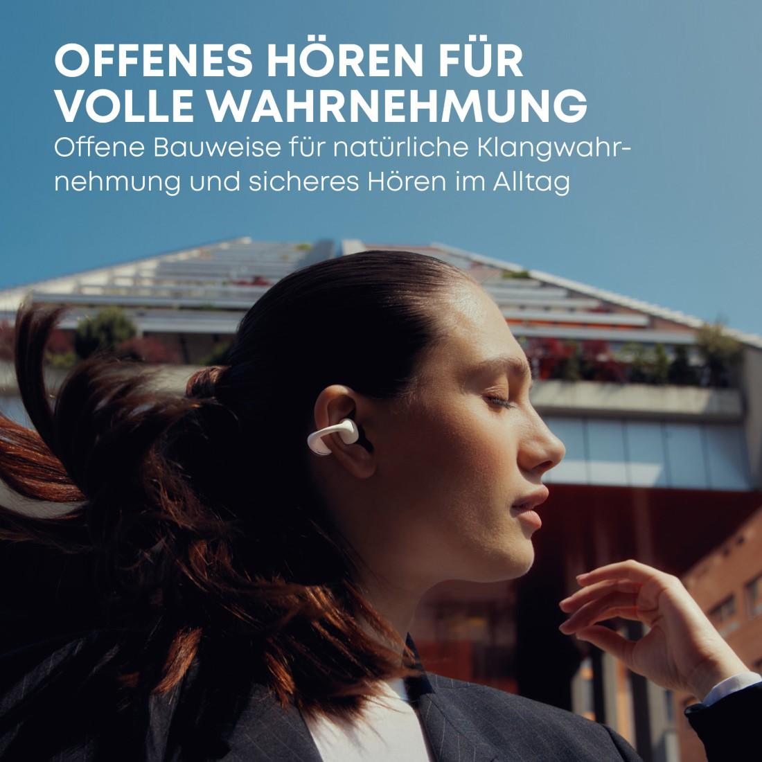 Frau mit weißen Ohrhörern, Seitenprofil. Text: Offenes Hören für volle Wahrnehmung. Gebäude und blauer Himmel im Hintergrund.