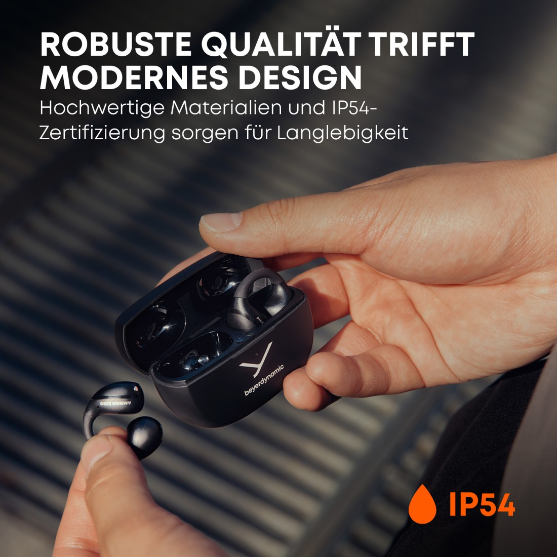 Eine Person hält ein schwarzes Ohrhörer-Etui. Im Etui befinden sich schwarze Ohrhörer. Der Text lautet 'ROBUSTE QUALITÄT TRIFFT MODERNES DESIGN'