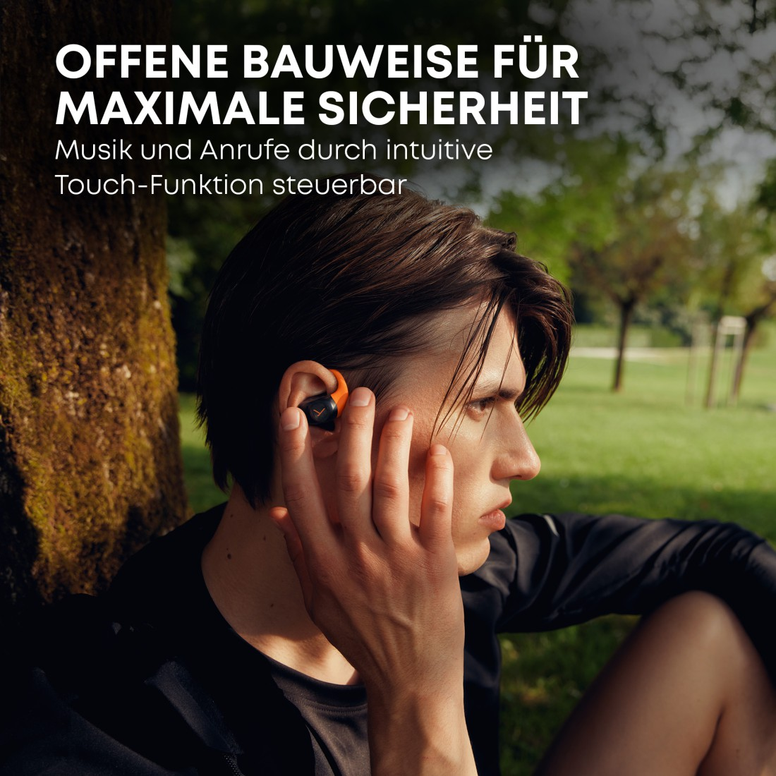 Ein Mann sitzt auf dem Gras und trägt ein schwarzes Hemd und orangefarbene Ohrhörer. Der Text darüber lautet: 'OFFENE KONSTRUKTION FÜR MAXIMALE SICHERHEIT'.