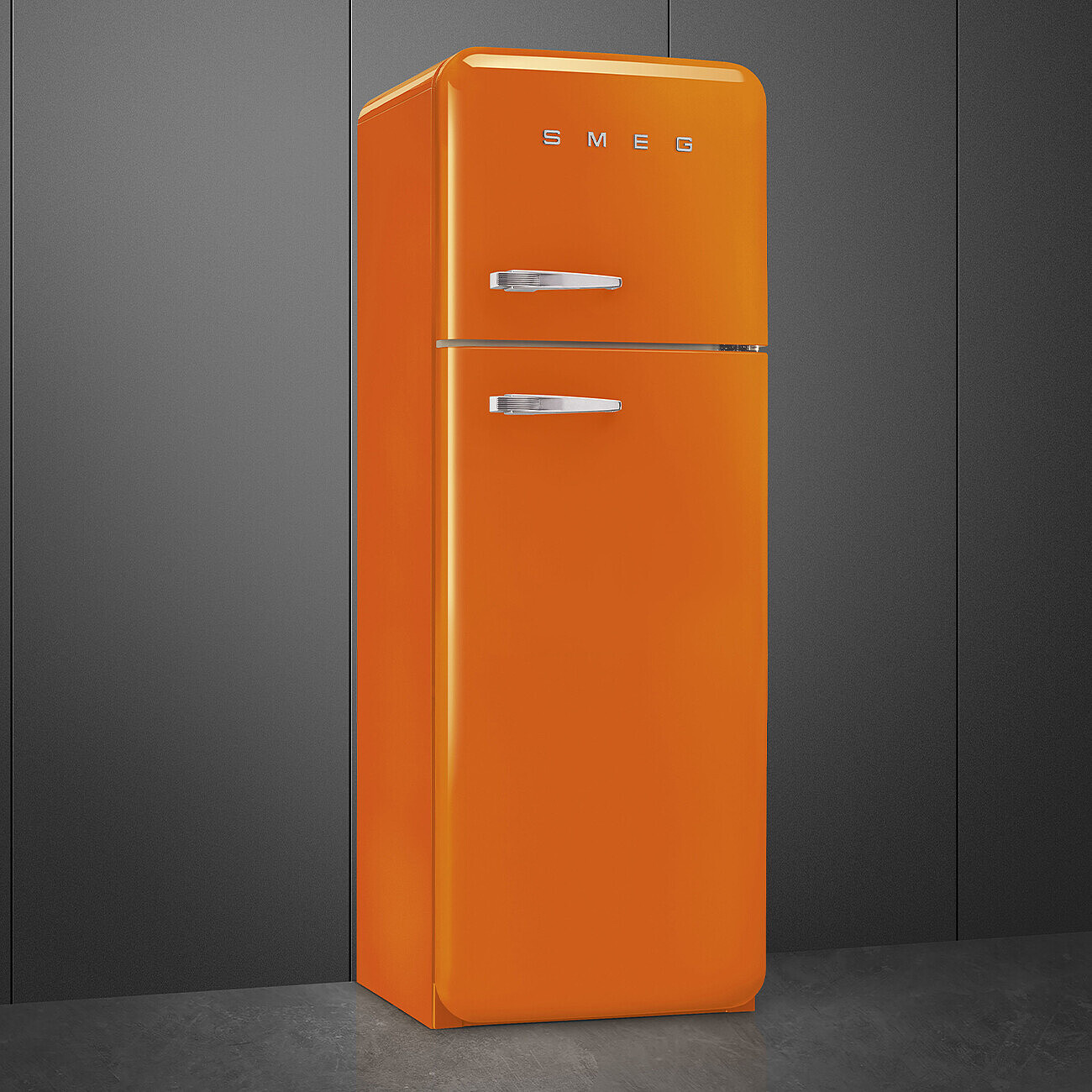 Ein orangefarbener Smeg-Kühlschrank steht vor einem dunkelgrauen Hintergrund. Chromgriffe und das Smeg-Logo sind sichtbar.