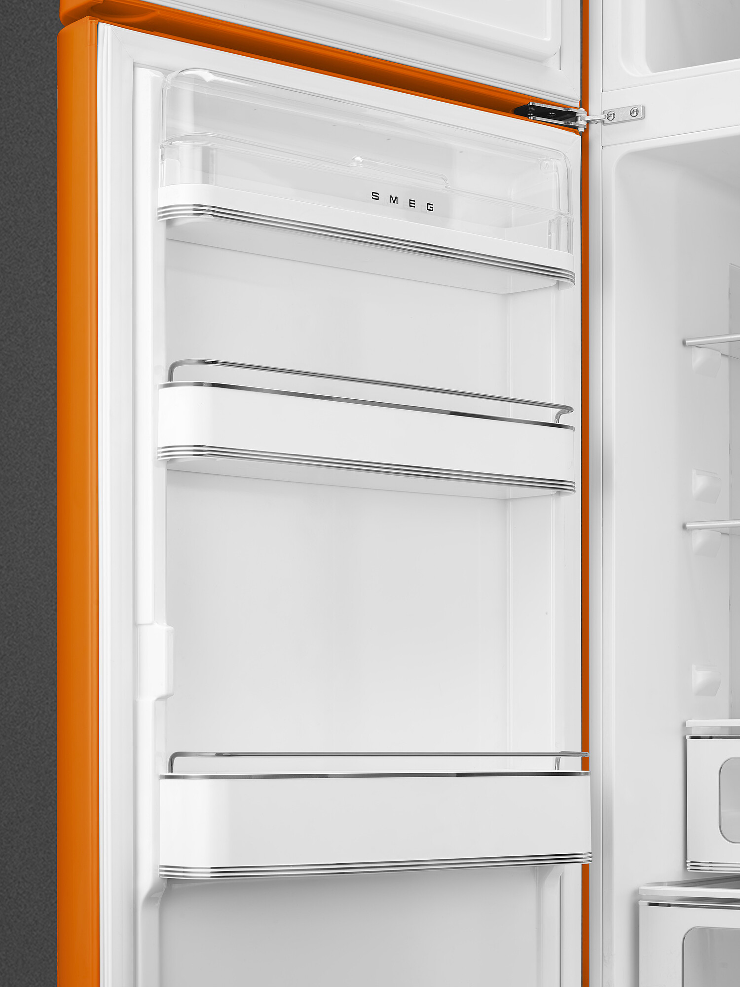 Offener orangefarbener SMEG-Kühlschrankinnenraum. Weiße Regale, transparente Türfächer. Oranger Rahmen, grauer Hintergrund.