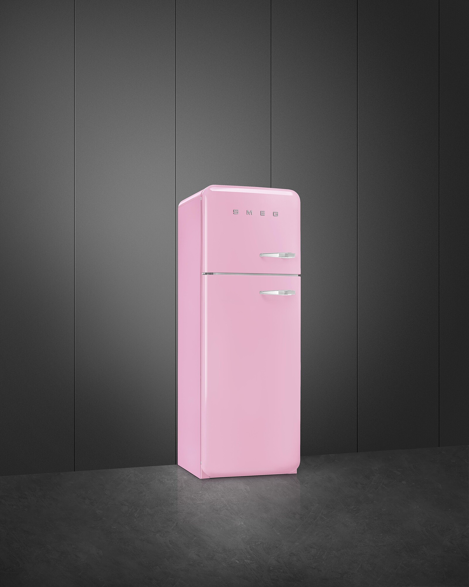 Ein rosafarbener SMEG-Kühlschrank steht vor einer dunkelgrauen Wand. Der Boden ist dunkelgrau.