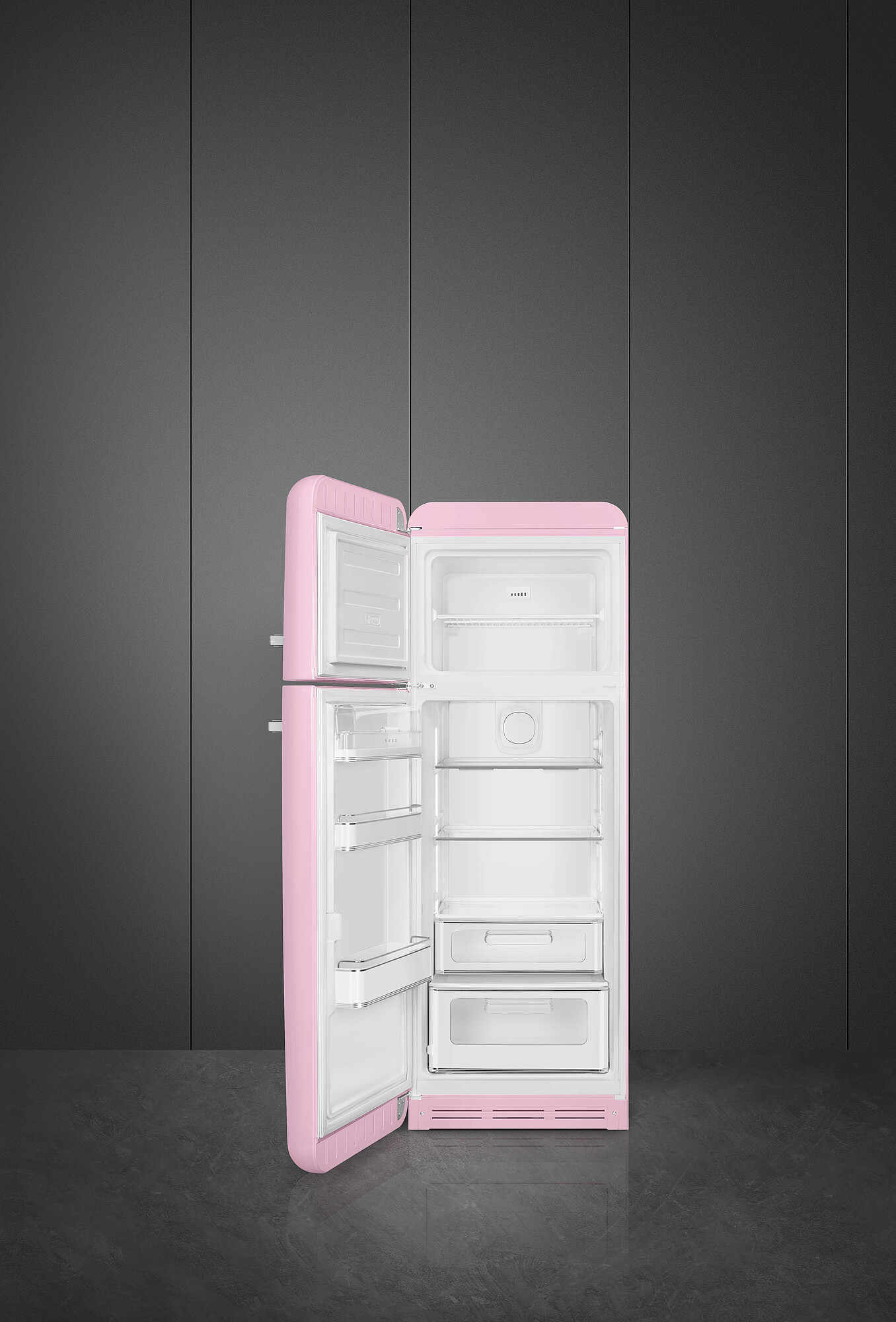 Ein rosafarbener Retro-Kühlschrank mit geöffneten Türen steht vor einer grauen Wand. Das Innere zeigt Regale und Schubladen.