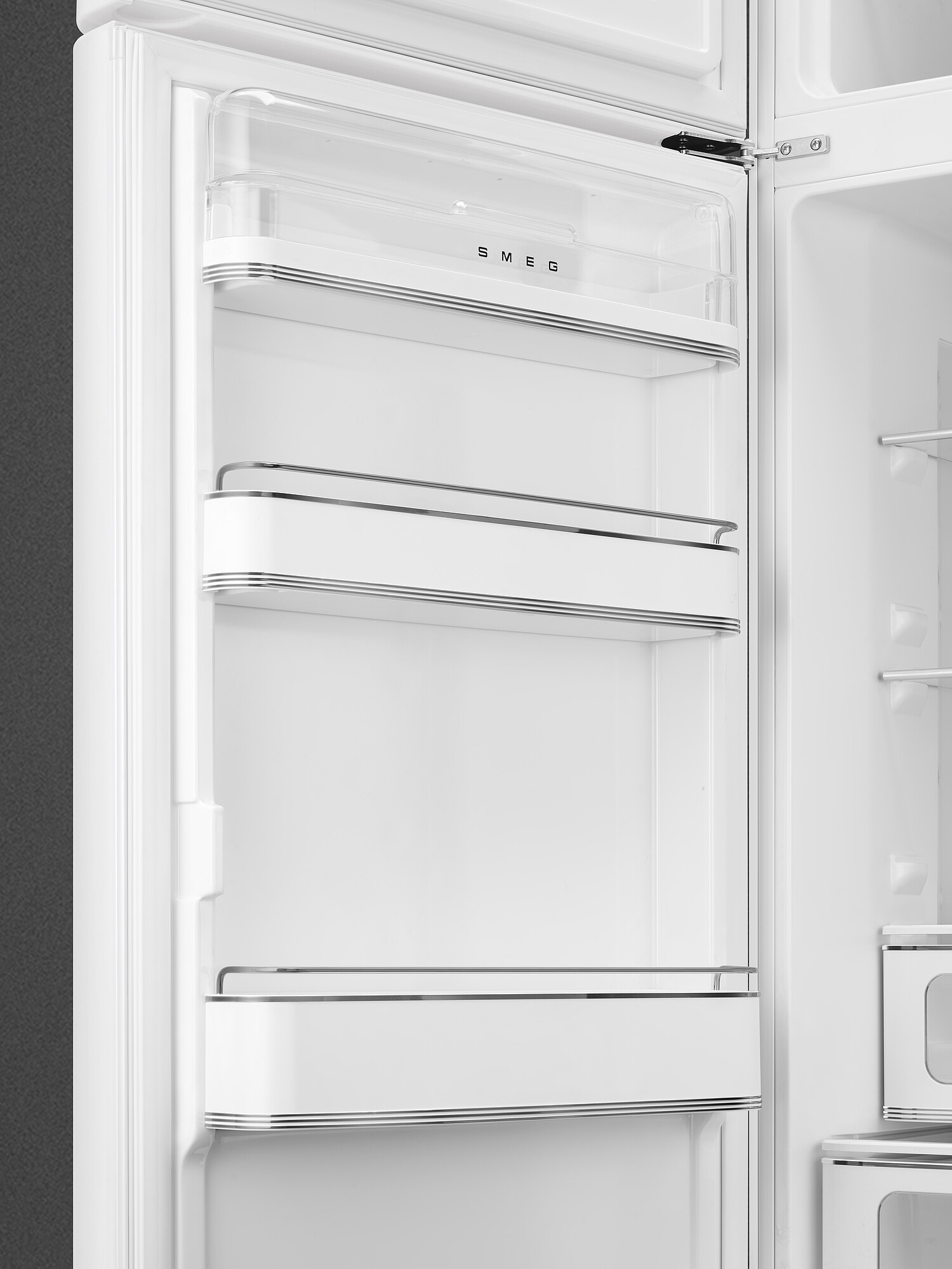 Offener weißer Kühlschrankinnenraum. Sichtbare Regale, Glastür. SMEG-Logo. Grauer Hintergrund links. Die Tür ist offen.