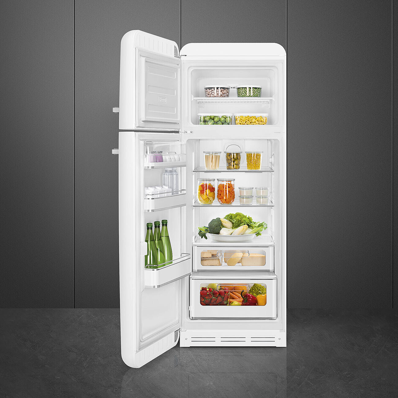 Offener weißer Kühlschrank mit Lebensmitteln gefüllt: Gemüse, Obst, Gläser. Die Tür ist geöffnet. Graue Wand und Boden.