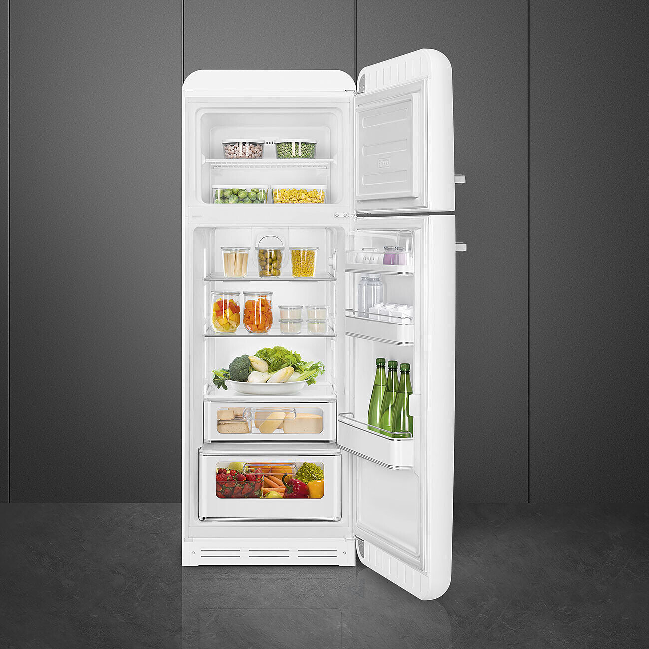 Offener weißer Kühlschrank gefüllt mit Lebensmitteln: Obst, Gemüse, Gläsern und Flaschen. Graue Wand im Hintergrund.