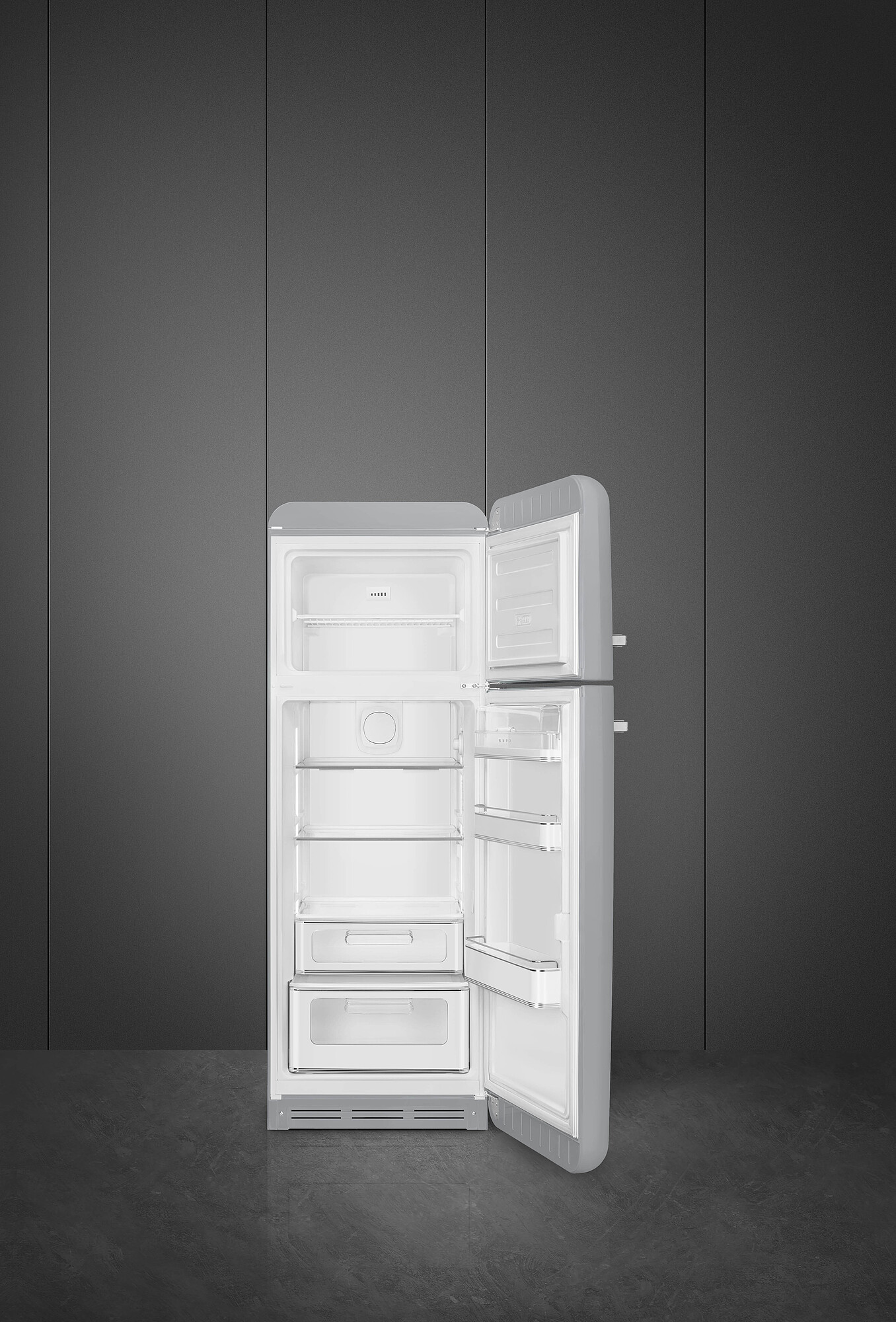 Offener, retro-grauer Kühlschrank vor einer dunkelgrauen Wand und einem dunklen Boden. Die Kühlschranktür ist geöffnet und zeigt Regale.