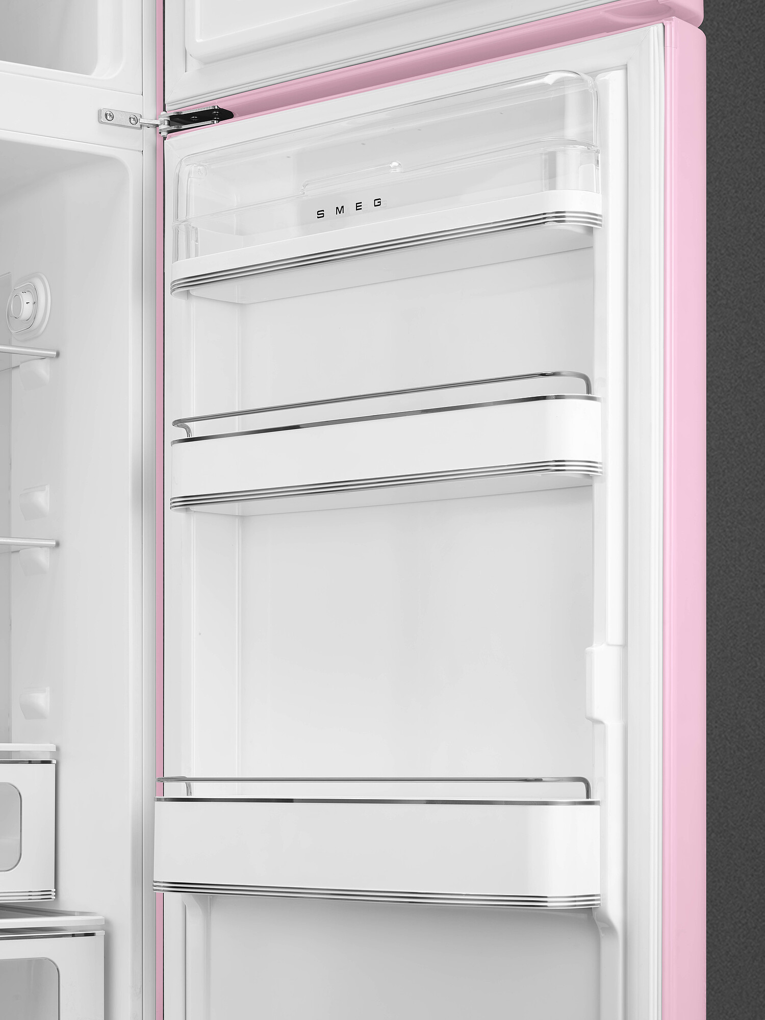 Offener rosa Smeg-Kühlschrankinnenraum. Weiße Regale mit Metallbesatz. Klare Plastikbox. SMEG-Logo. Grauer Hintergrund.