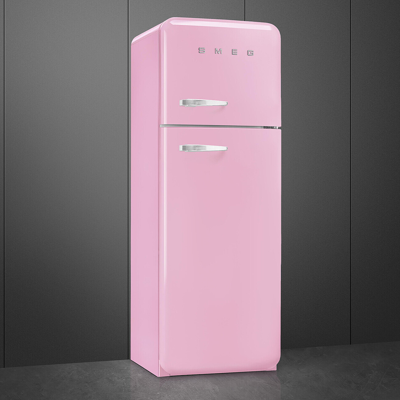 Ein rosafarbener Smeg-Kühlschrank mit silbernen Griffen vor einer dunkelgrauen Wand und einem grauen Boden.