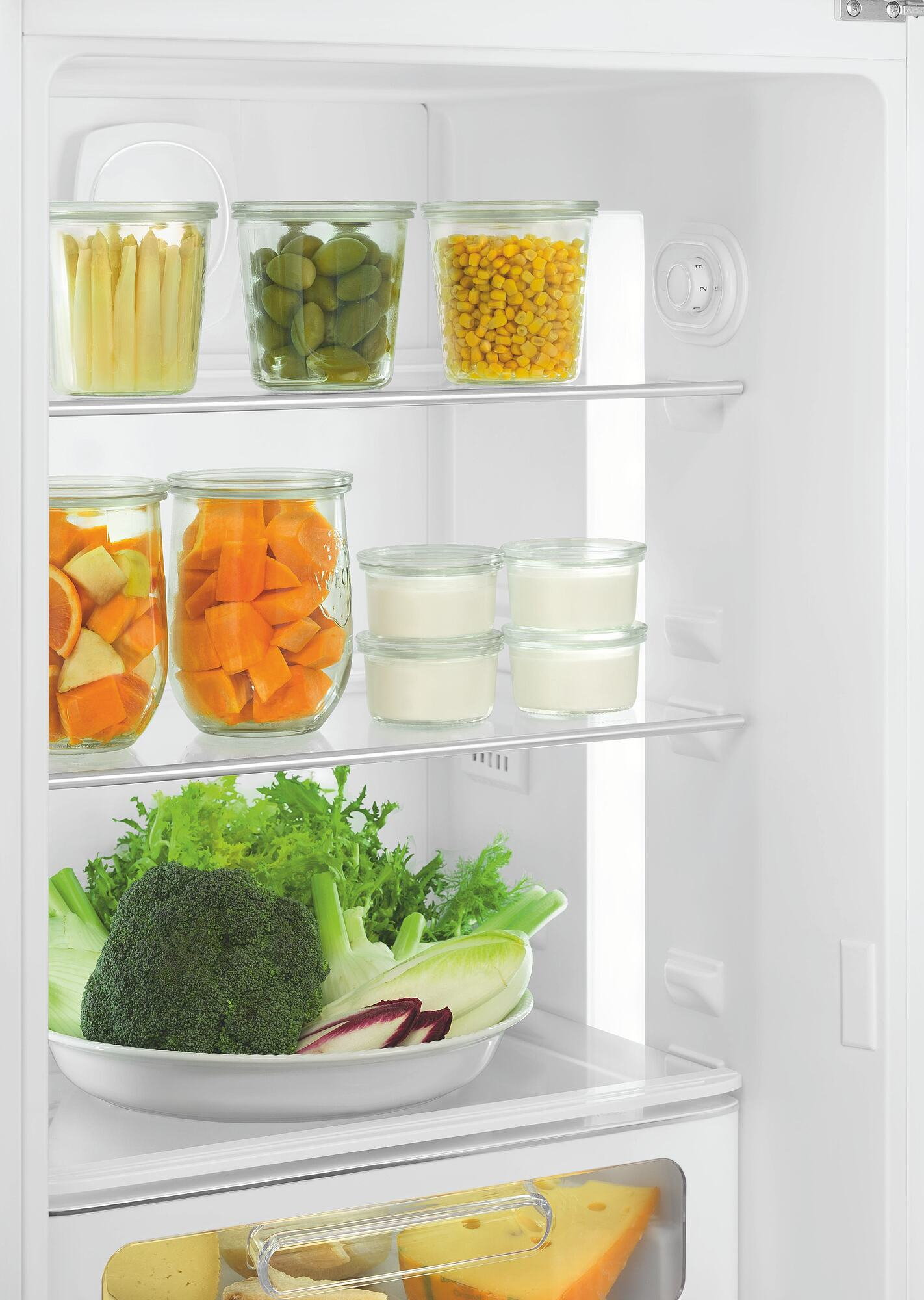 In einem Kühlschrank: Gläser mit Spargel, Oliven, Mais, Orangen, Kürbis, Joghurt. Brokkoli und Salat. Käse unten.