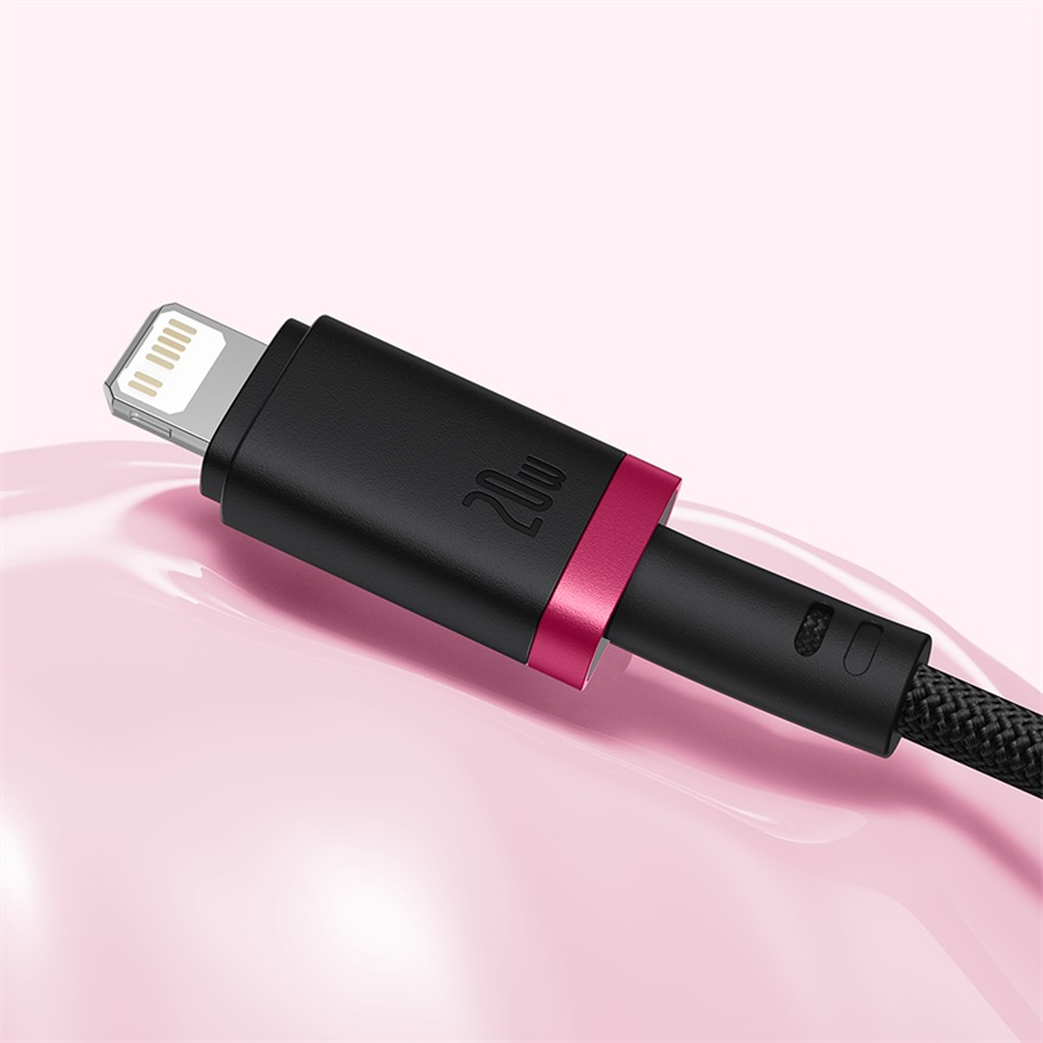 Primer plano de un cable de carga negro con conector Lightning, anillo rosa y cable trenzado sobre fondo rosa.