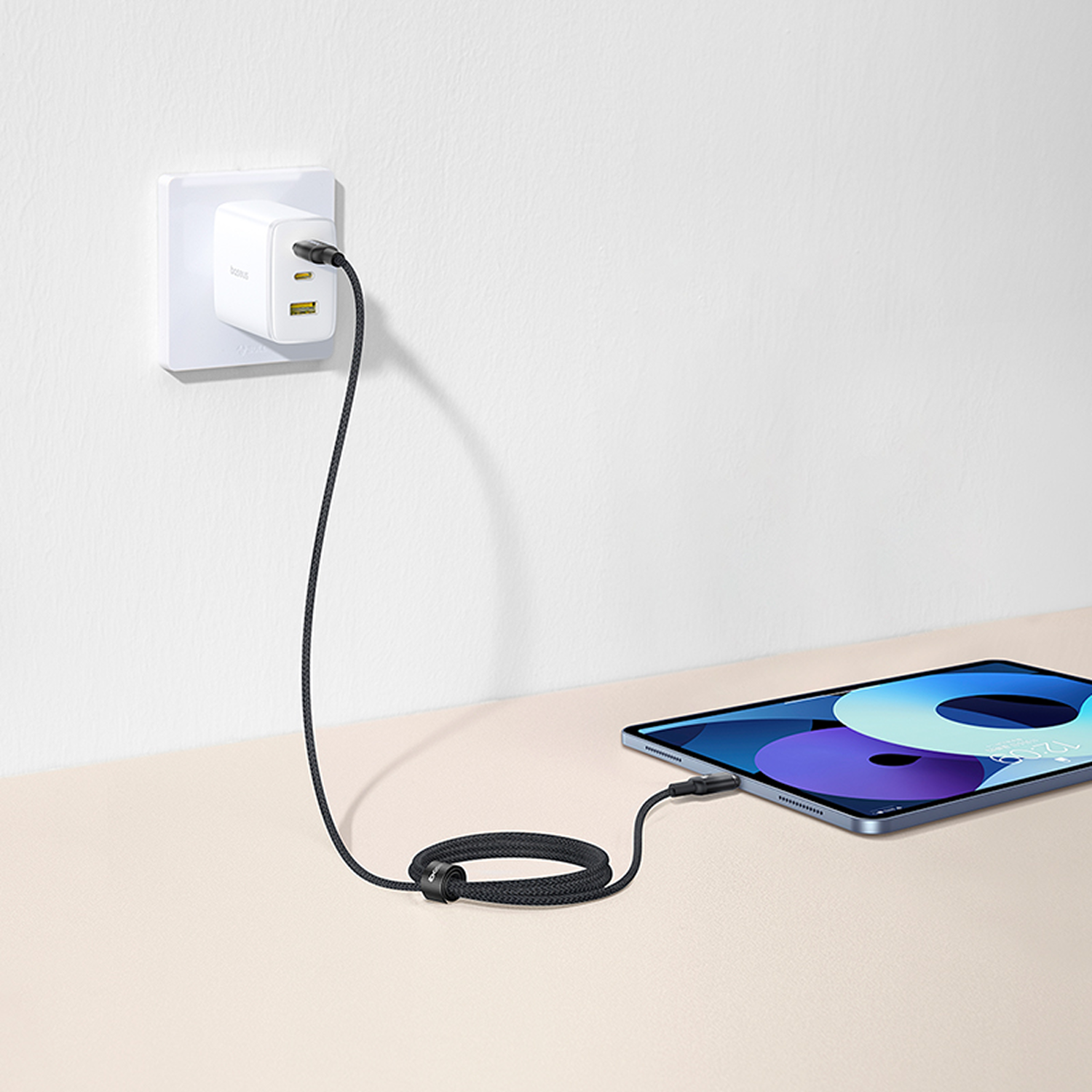 Tableta cargando con un cable negro conectado a un cargador de pared blanco. La tableta está sobre una superficie beige.
