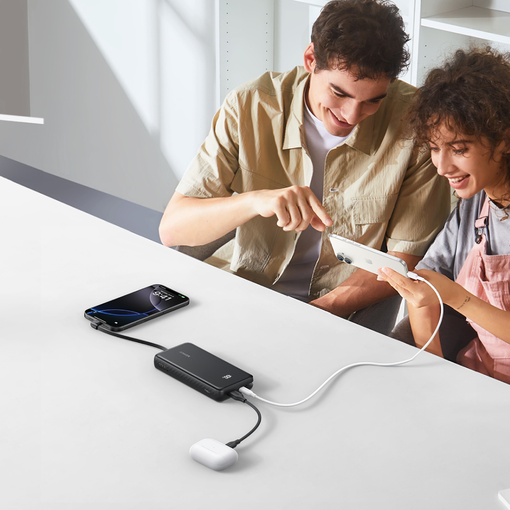Zwei Personen betrachten ein Telefon, das mit einer Powerbank verbunden ist. Ein weiteres Telefon und Ohrhörer sind ebenfalls angeschlossen.