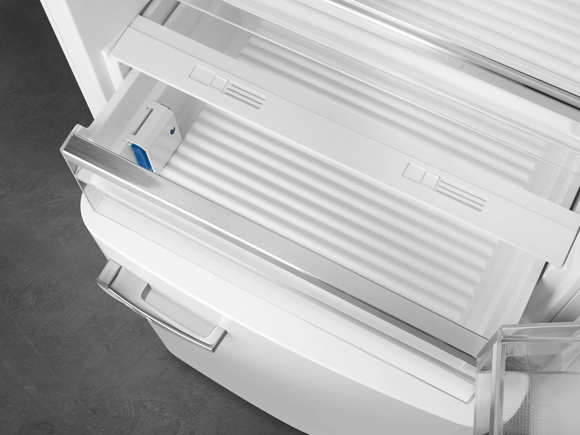 Offene weiße Kühlschublade mit Metallgriff. Blaues und weißes Objekt innen. Grauer Boden. Sauberes, modernes Design.