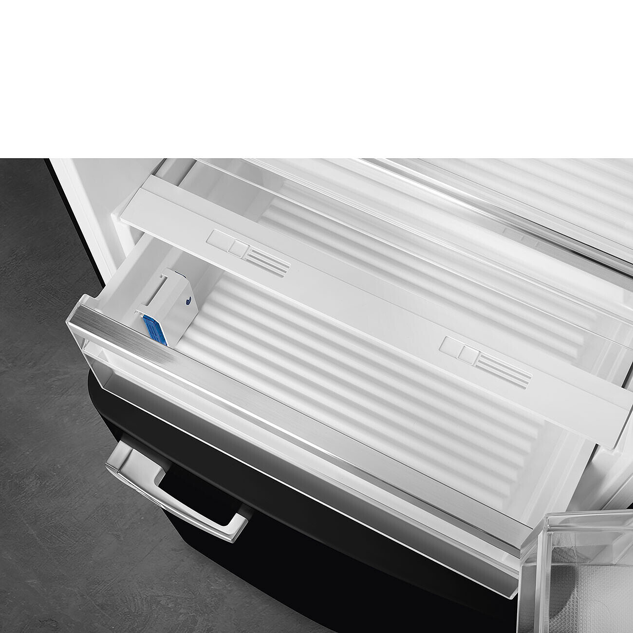 Offene Kühlschrank Schublade. Weiße Schublade mit silberner Verkleidung. Blaues Gerät innen. Schwarzer Kühlschrank und grauer Boden.