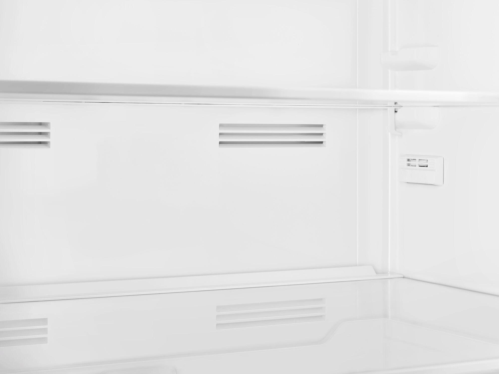 In einem weißen Kühlschrank, leer. Merkmale sind Regale, Lüftungsschlitze und ein Bedienfeld. Die Gesamtästhetik ist sauber und minimalistisch.