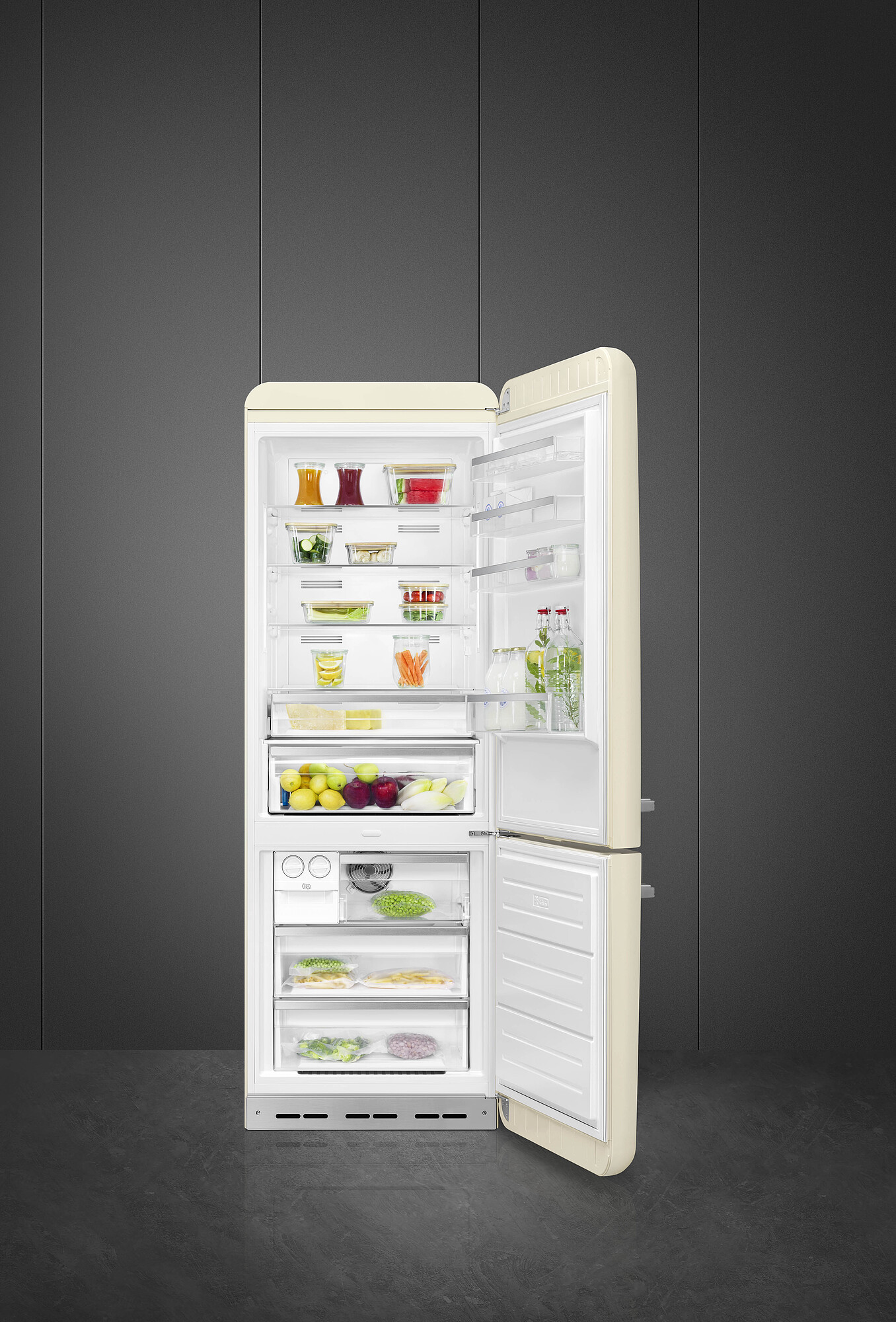Offener cremefarbener Kühlschrank mit Lebensmitteln gefüllt. Enthält Früchte, Gemüse und Fertiggerichte. Dunkelgraue Wand dahinter, grauer Boden.