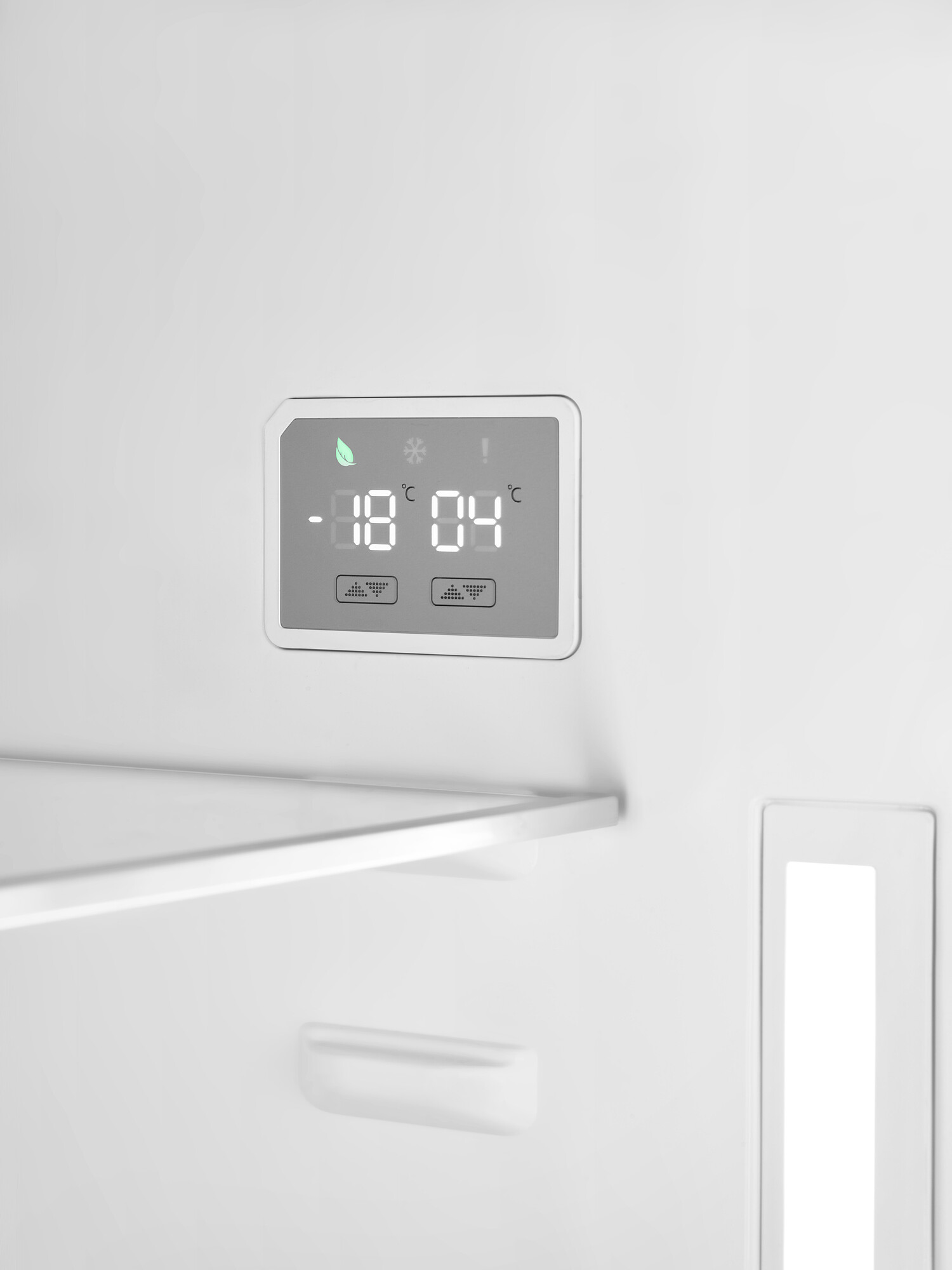 In einem weißen Kühlschrank zeigt ein digitales Display -18°C und 4°C an. Ein Regal ist sichtbar. Die Tür hat ein weißes, vertikales Fach.