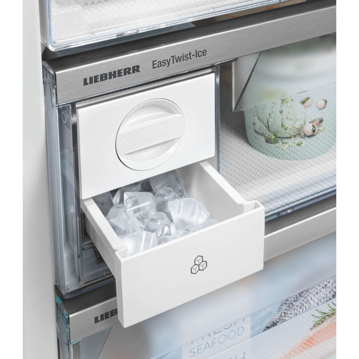 A white ice maker drawer is open, filled with ice cubes. Above it, a dial. The brand name LIEBHERR is visible. Background shows other fridge parts.