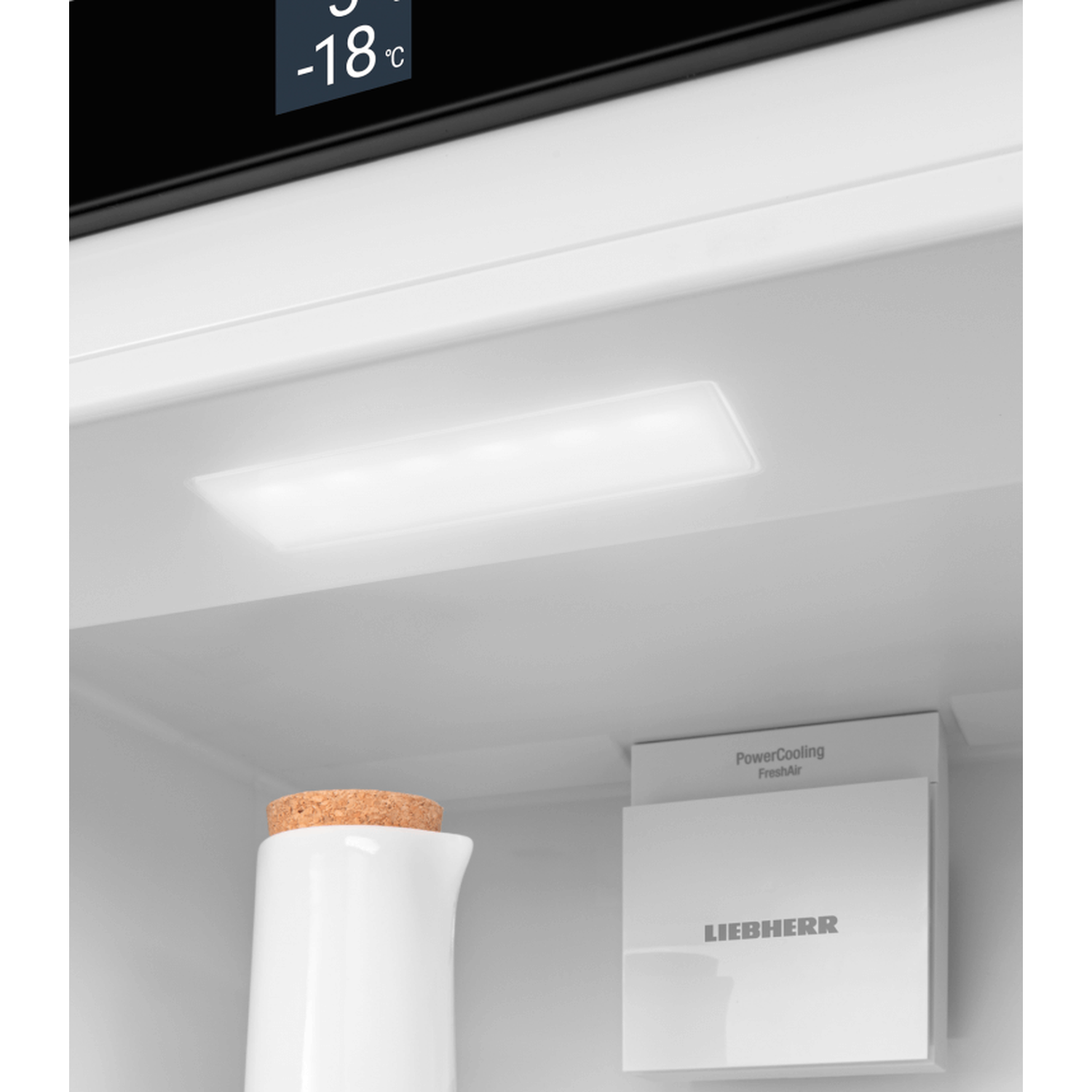 Inside a fridge: white pitcher with cork, light, and Liebherr FreshAir system. Temperature display shows -18°C.
