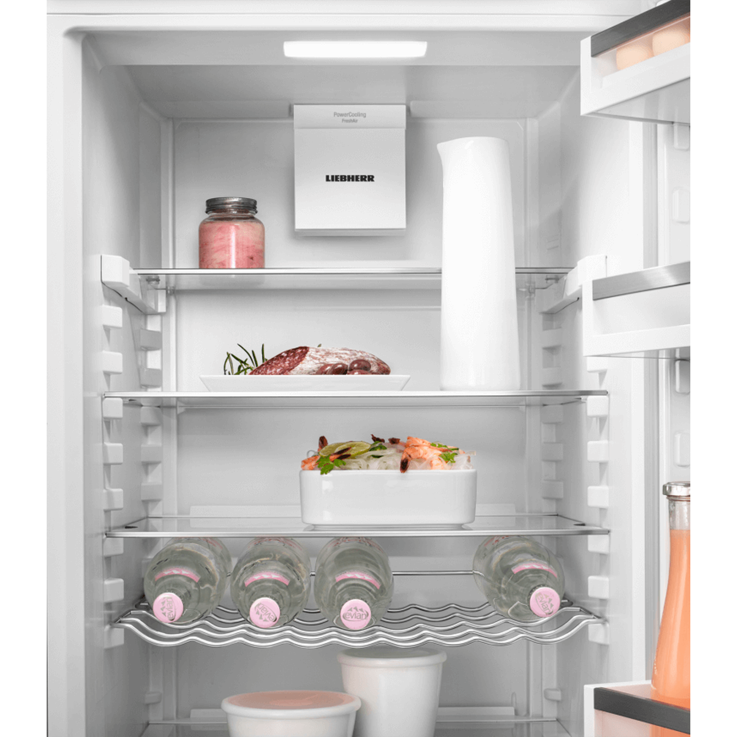 Inside a refrigerator, there is food and drinks. There are bottles of water, a jug, and some containers with food.