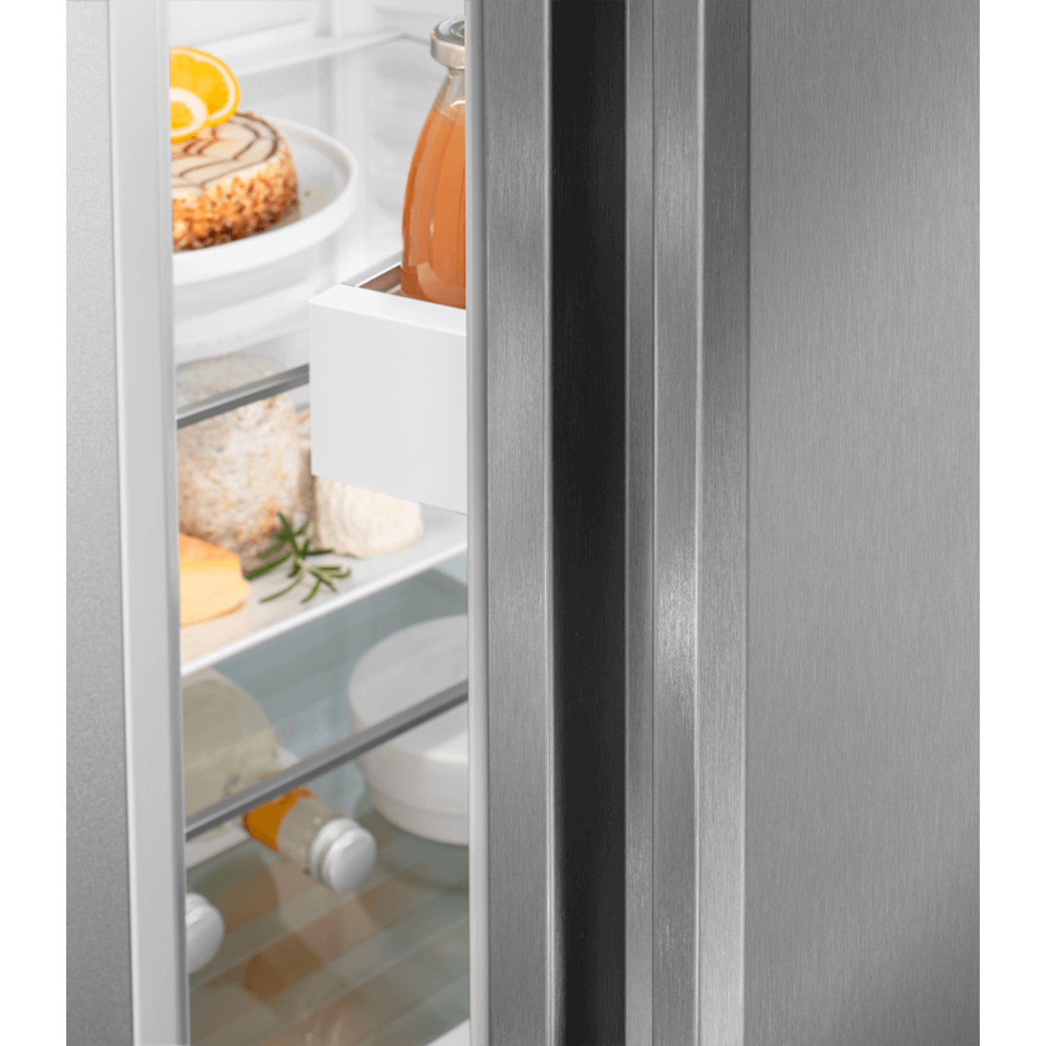 Open refrigerator with food inside. Includes cake, cheese, juice, and other items. Stainless steel door is on the right.