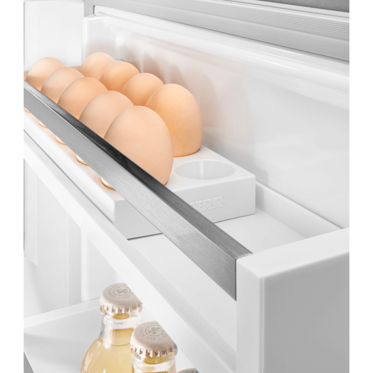 Inside a refrigerator, a row of brown eggs sits on a shelf. Below, two glass bottles with golden liquid are visible.
