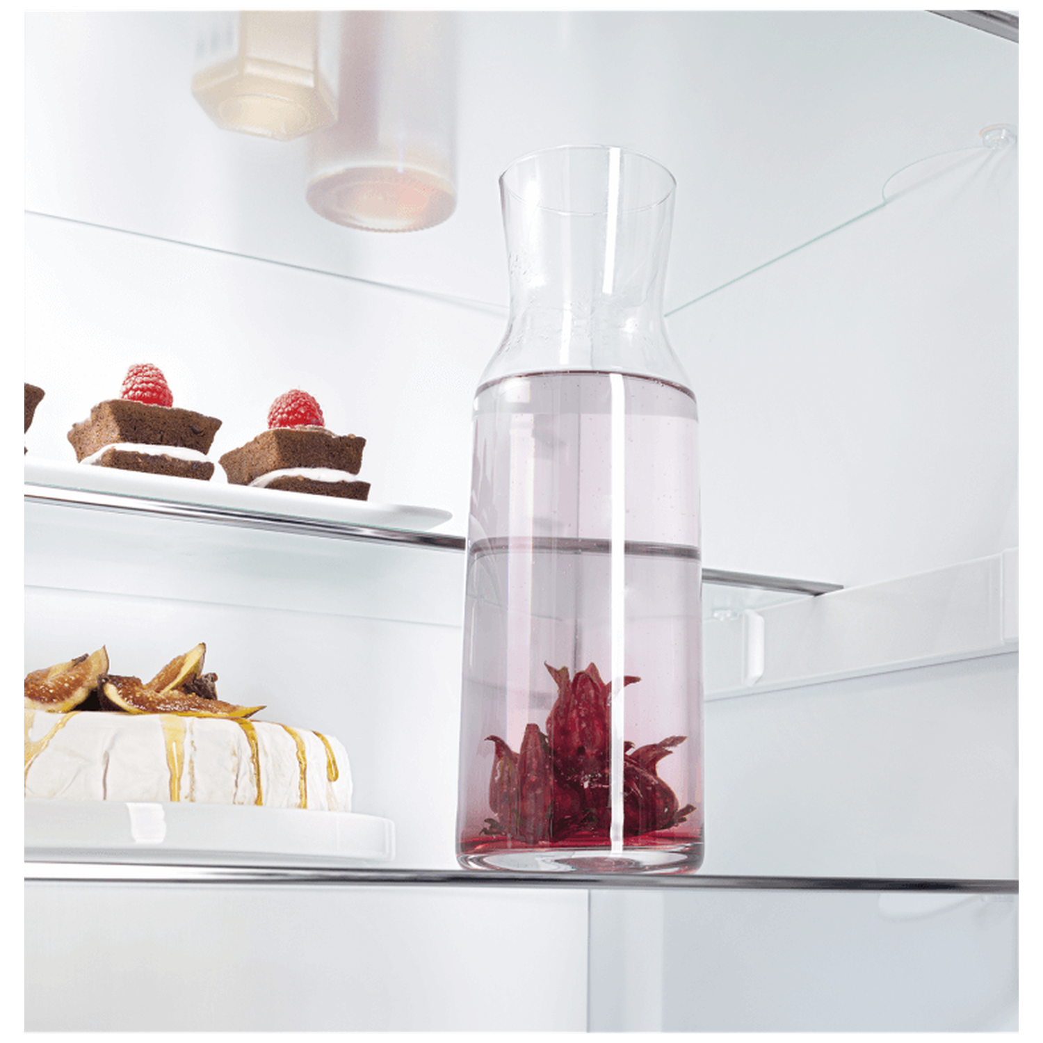 Inside a fridge: a glass carafe with infused water, cakes with raspberries, cheese with figs and honey.