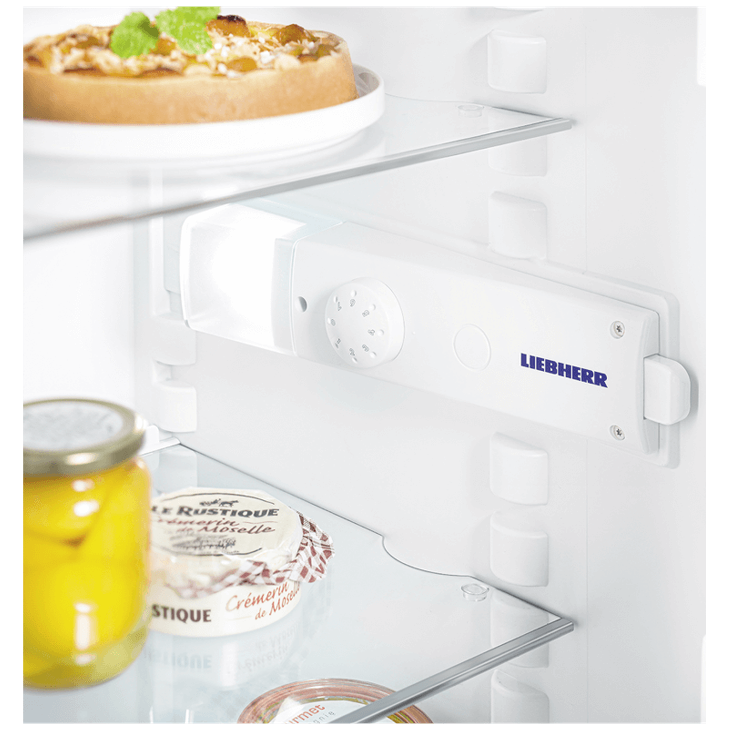 Inside a refrigerator: pizza, jar of yellow food, cheese, and Liebherr logo on white interior. Glass shelves are visible.